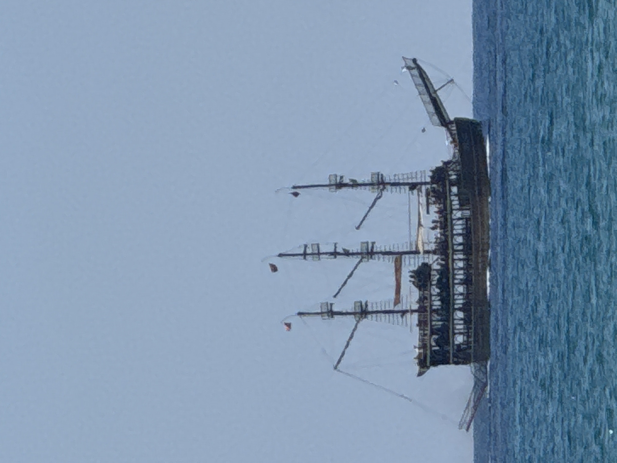 A three-masted sailing ship, resembling a pirate ship, is sailing on the Mediterranean Sea near Manavgat, Turkey. The ship has multiple decks and is crowded with people. It is a sunny day with a clear blue sky and calm turquoise water. The ship is the main subject of the image, which appears to be taken from a distance.