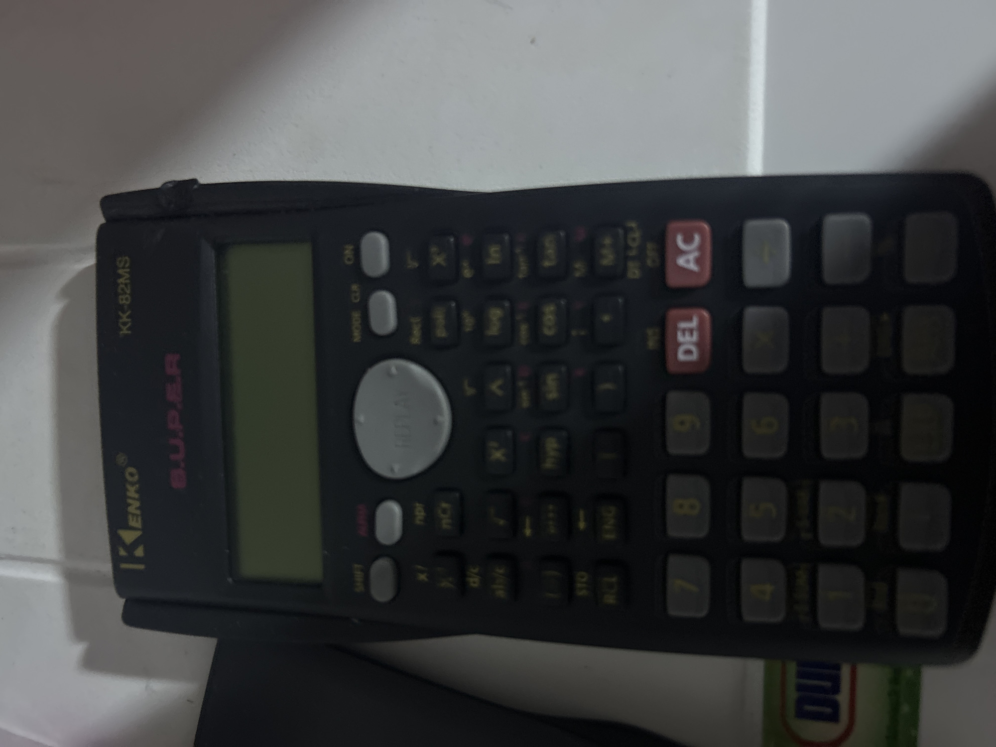 A black Kenko KK-82MS calculator is lying on a white surface. The calculator has a display screen and several buttons. It is a scientific calculator. The image provides no information about the location in San Juan de Los Morros, Venezuela, or any people, actions, or interactions.