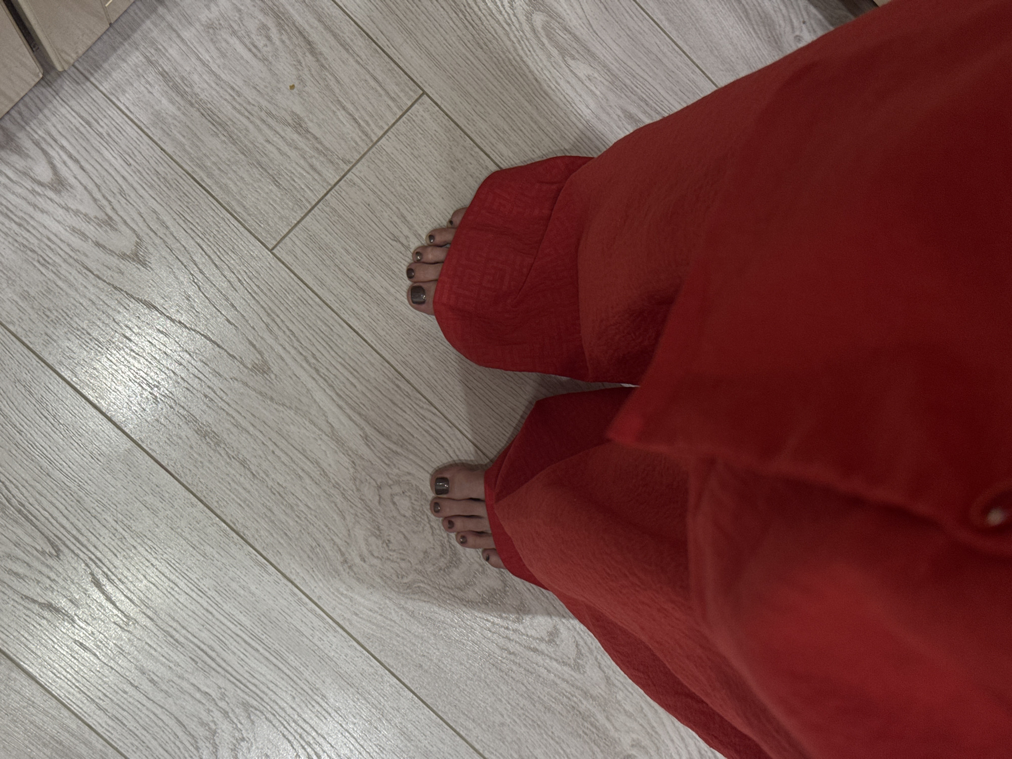 A high-angle shot depicts two feet on a light wood-look floor, partially covered by red fabric. The toes are visible, with dark nail polish. The setting appears to be indoors. There's no indication of the city of Izhevsk, Russia in the image.