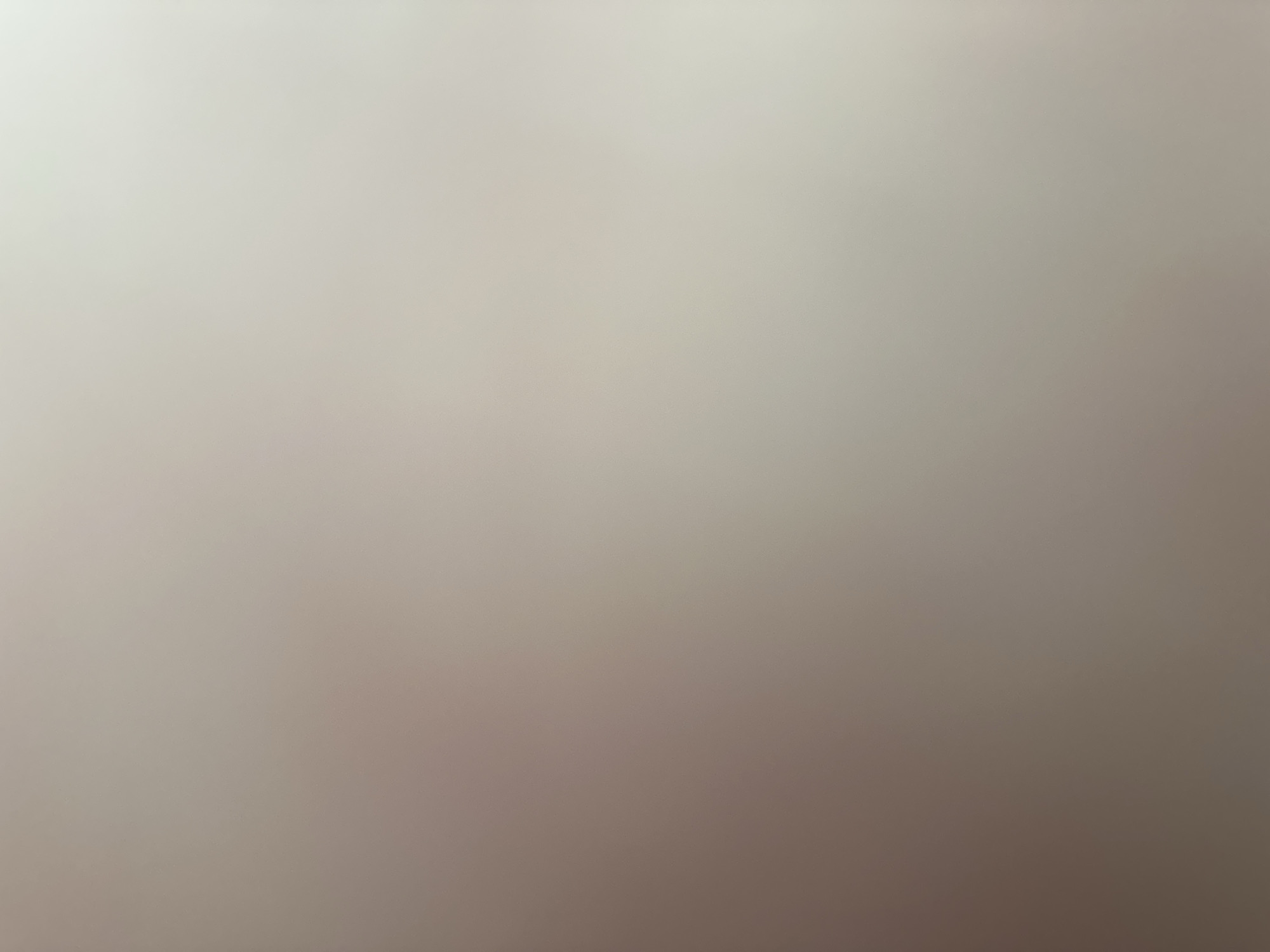 The image is an out-of-focus abstract depiction with a smooth gradient of colors ranging from a very light, almost white tone at the top to a darker, warmer brownish-gray at the bottom. There are no discernible subjects, objects, or scene details. No activity or event is taking place. There are no notable details such as time of day, weather, location cues, or emotions. No text is visible. The image appears to be a digital artifact or a photograph taken of a uniform, out-of-focus surface.