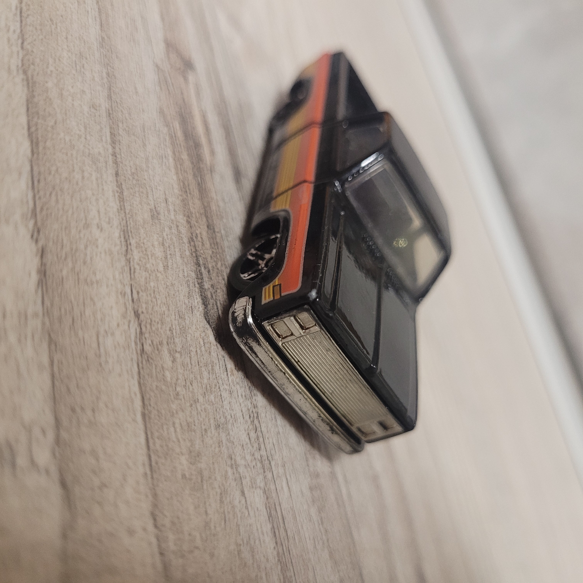 A black toy truck with orange and yellow stripes on the side is on a wooden surface. The truck is a pickup truck with a chrome grill and bumper. The truck's wheels are visible.