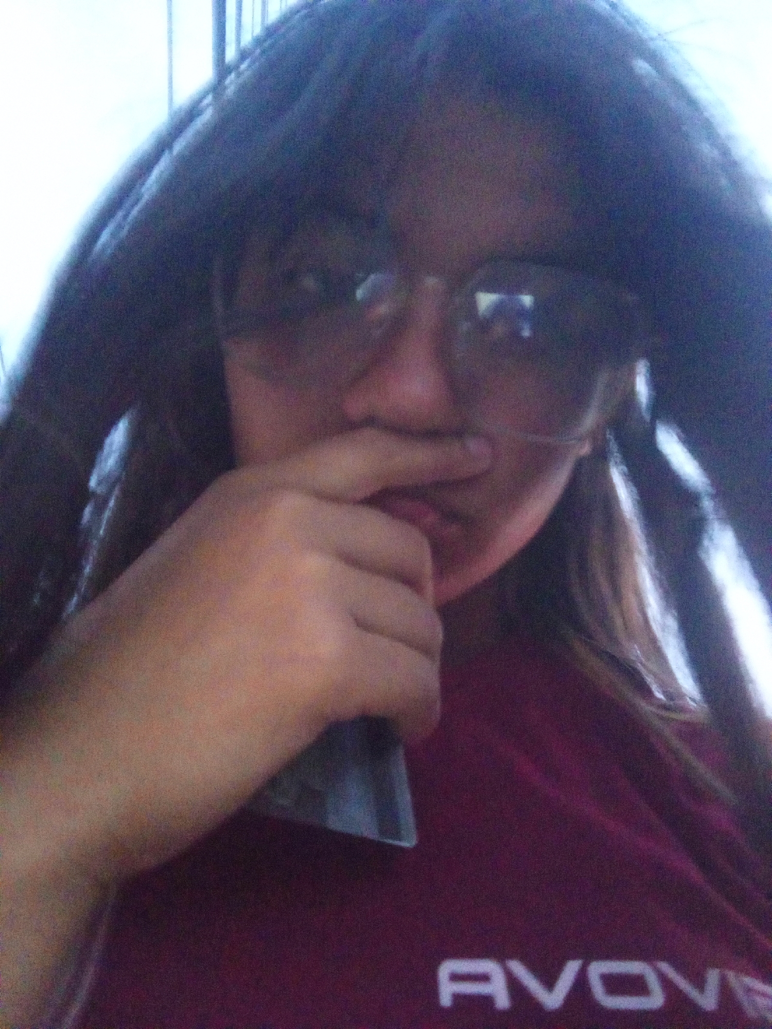 A close-up selfie depicts a person wearing dark sunglasses, a dark burgundy t-shirt with "AVOVE" printed in white, and whose left hand is held near their mouth. The person has dark hair and appears to be indoors with natural light. There is no evidence of the location being in Juan Griego, Venezuela in the image.