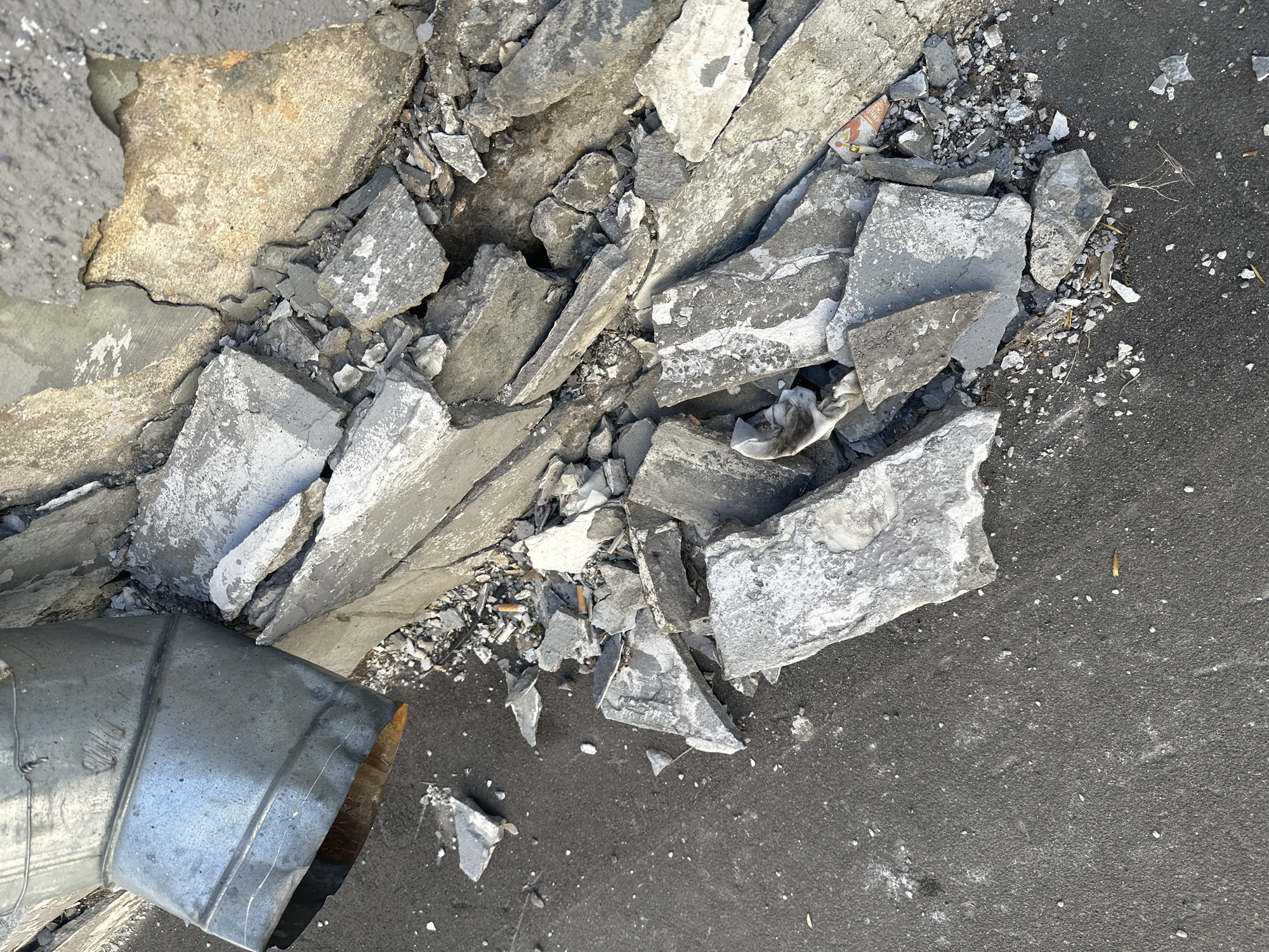 The image shows debris from broken concrete, including large fragments and fine gravel, scattered on an asphalt surface. A section of galvanized metal ductwork lies partially within the debris field. The setting appears to be an outdoor area. Based on the user's prompt, the location is in the city of Moscow, Russia. No people are visible. The scene suggests recent demolition or damage to a concrete structure.