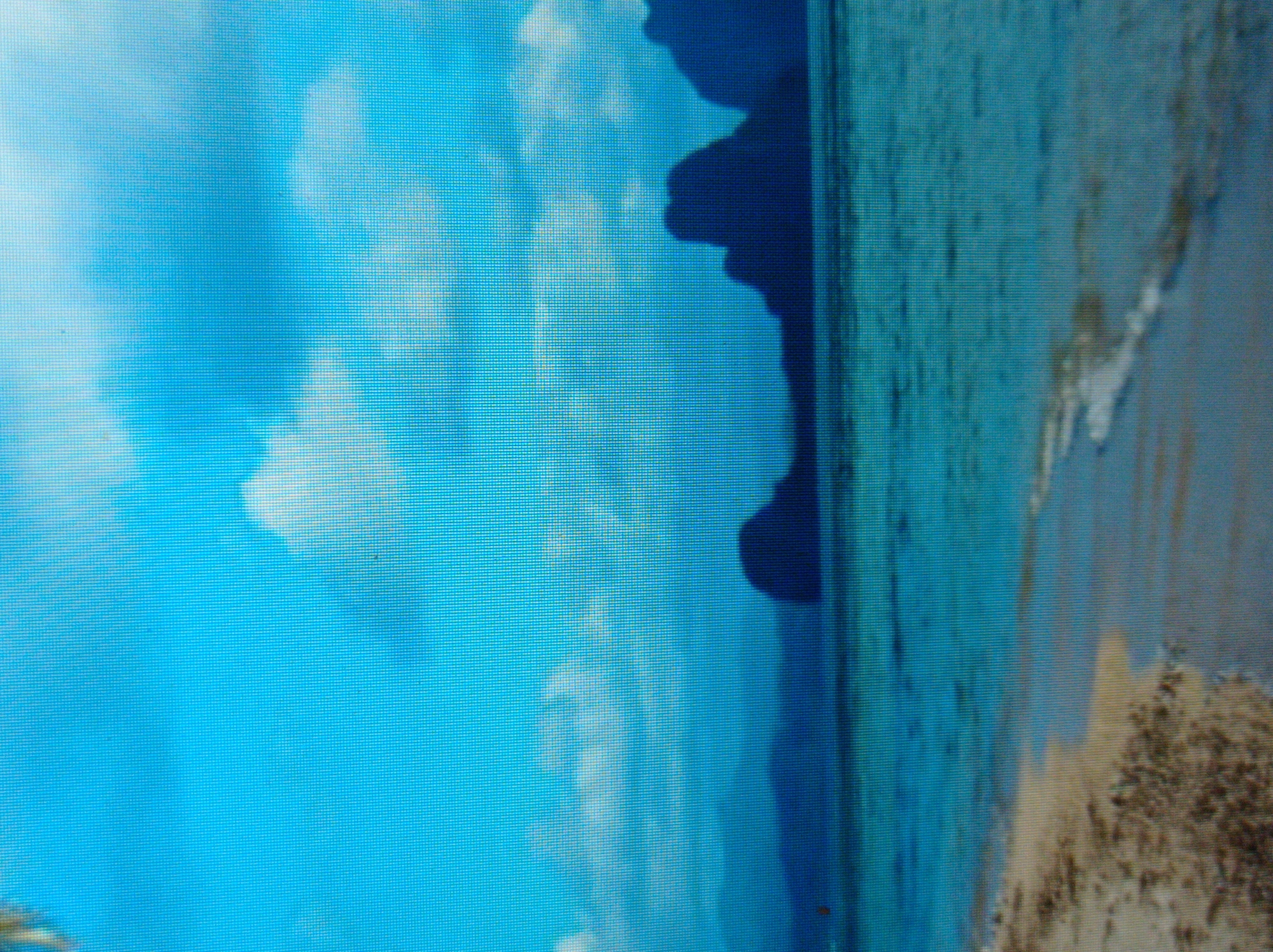 The image depicts a serene beach scene with calm, turquoise waters meeting a sandy shore. In the background, silhouetted against a vibrant blue sky with scattered clouds, are several large, dark rock formations, possibly islands or cliffs. The overall impression is one of natural beauty and tranquility. There are no people, structures, or any identifiable elements that would suggest a connection to the city of Mukachevo, Ukraine. The image appears to be a landscape photograph of a coastal or island location.
