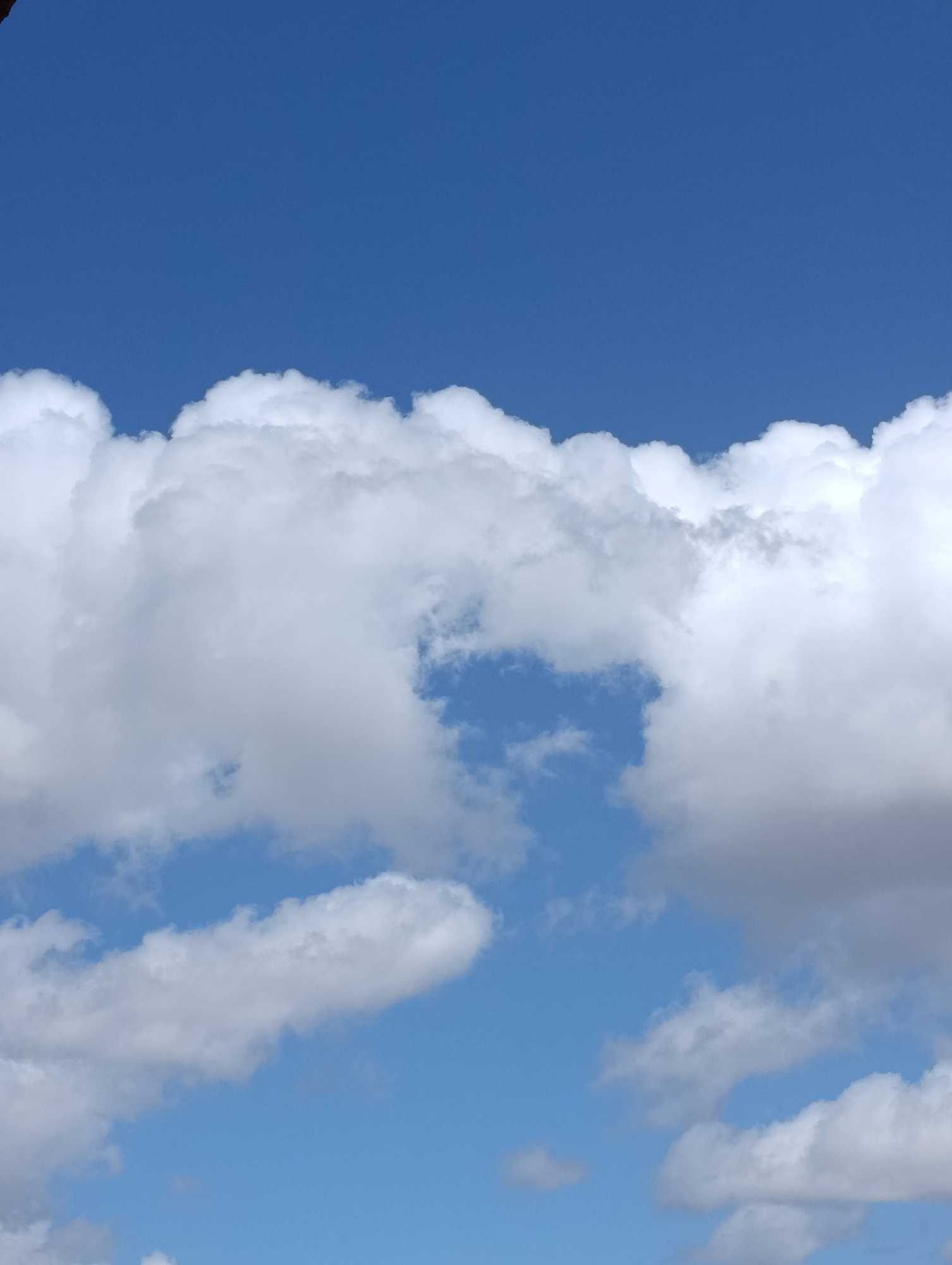 The image is an outdoor photograph of a blue sky filled with scattered white clouds. The clouds vary in size and density, with some appearing fluffy and others more wispy. The lighting suggests it is daytime. There are no people, structures, or recognizable landmarks visible in the image, making it impossible to determine a specific location within Setúbal, Portugal, or any city. The photograph focuses solely on the sky and clouds.