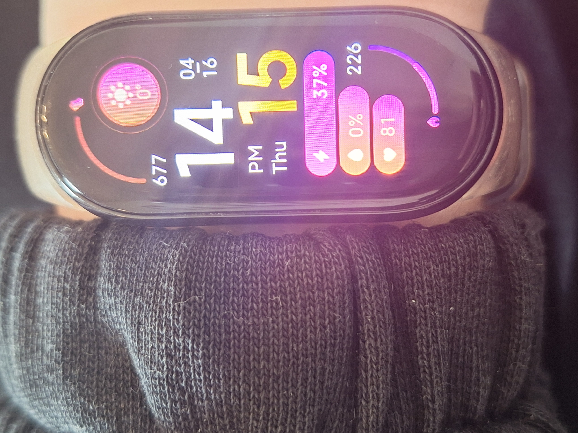 The image shows a smartwatch displaying the time as 14:15 (2:15 PM) on Thursday, April 16th. The watch face also indicates the following data: 677 steps taken, 6 hours of sleep, 37% battery life, 0% stress level, and a heart rate of 81 beats per minute. The smartwatch is worn on a wrist covered by a gray, knitted sweater sleeve. There is no information to conclude that the picture was taken in Chaikovsky, Russia.