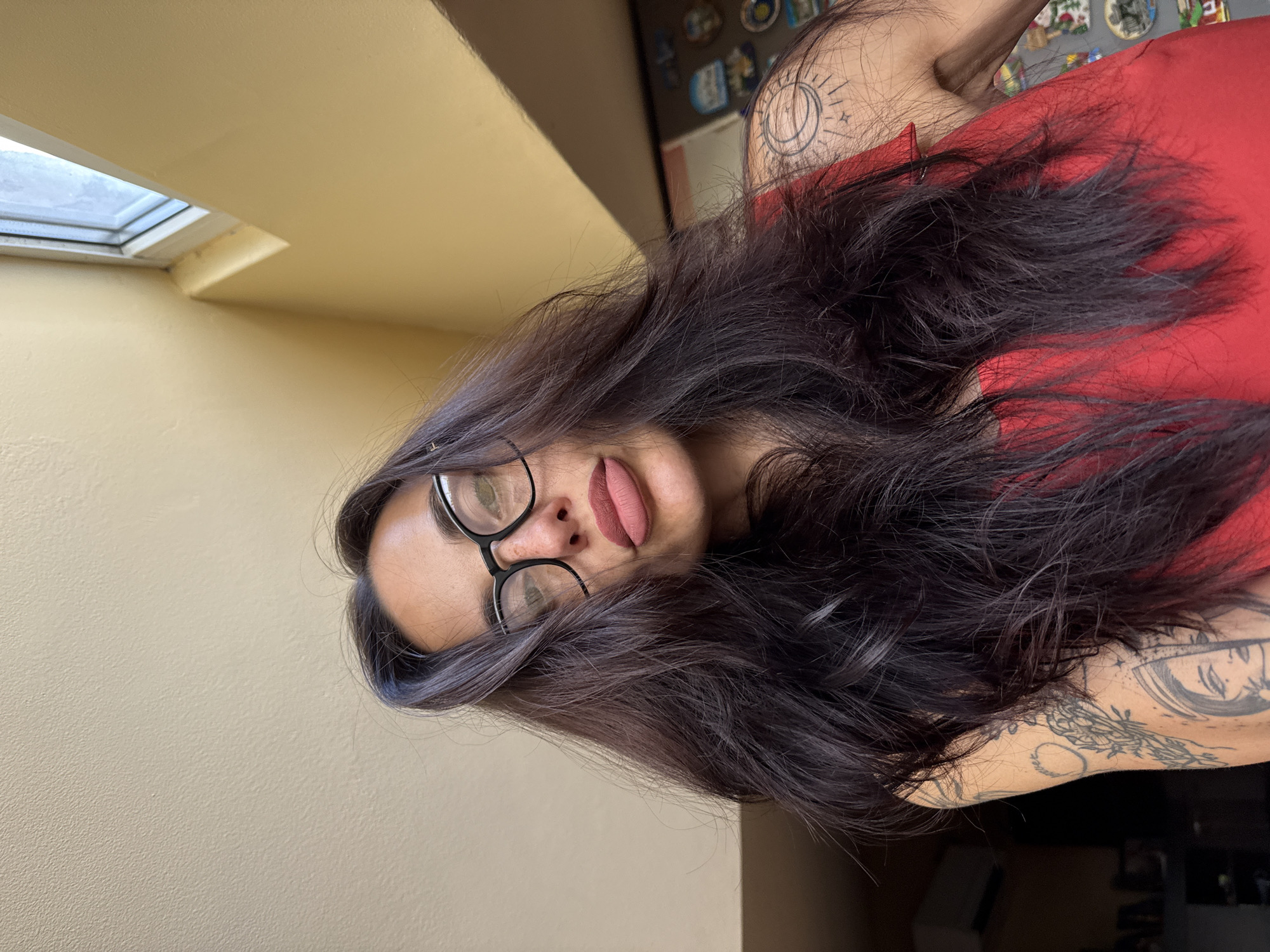 A woman with long, dark hair and glasses is posing for a photo indoors. She is wearing a red shirt. A skylight is visible in the background. Her arm is tattooed. The location is possibly in the city of Pleven, Bulgaria, though there are no specific details visible in the image to confirm this.