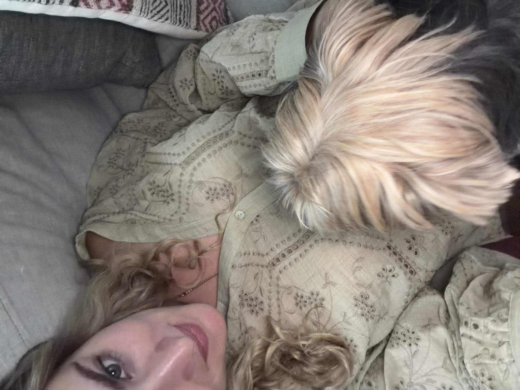 A selfie shows a person with blonde hair lying down, wearing a light-colored, patterned shirt. A dog with tan and black fur is lying next to them. They appear to be on a bed or couch, with pillows visible in the background. There are no visual cues indicating the specific location of San Bernardino Tlaxcalancingo, Mexico.
