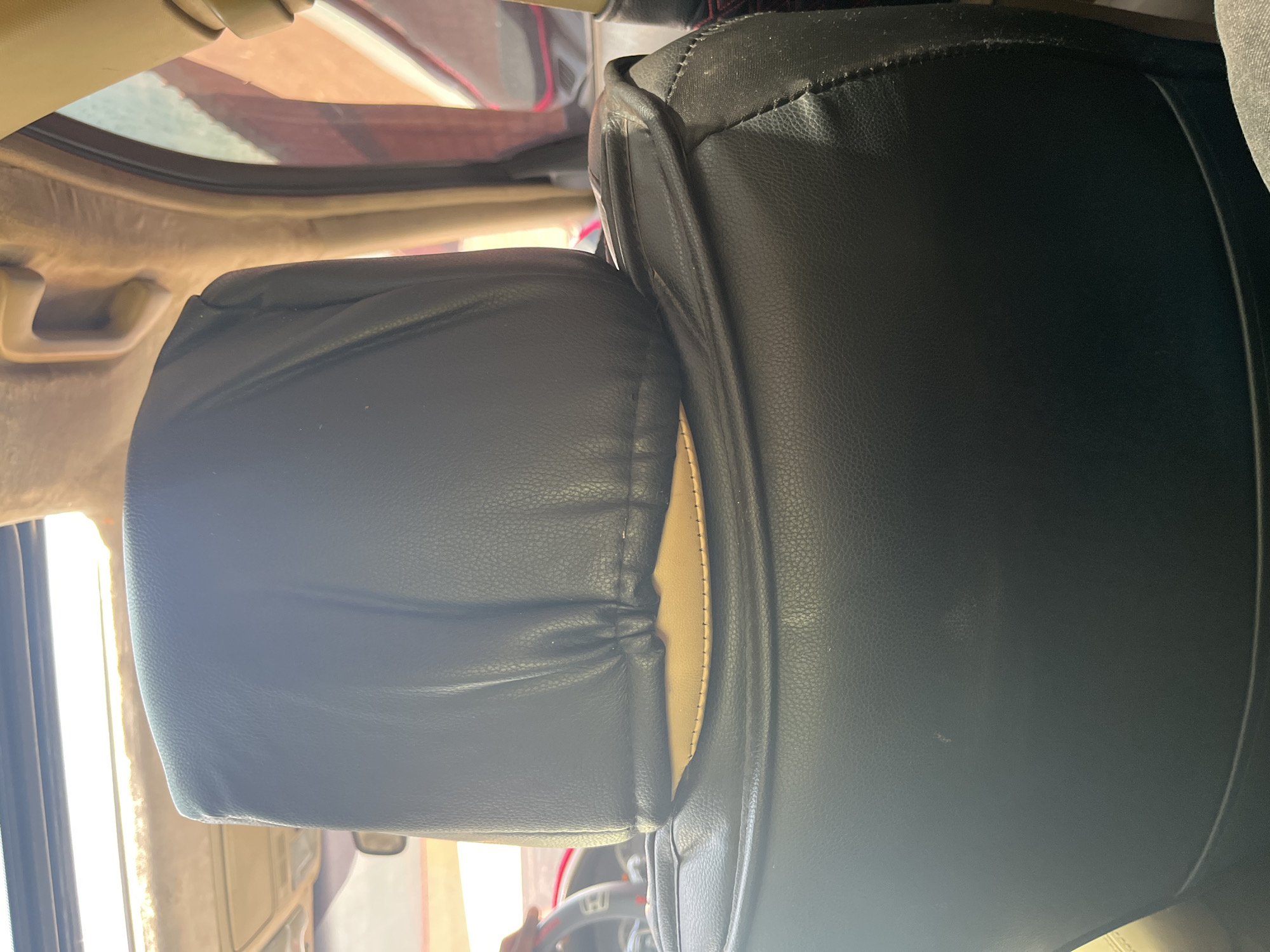 The image shows the interior of a car, specifically the headrest and upper portion of a car seat. The headrest is covered in black material with a lighter colored material visible underneath near the bottom. The seat itself is also covered in black material. The ceiling of the car is visible at the top, with a sunroof or skylight. The image appears to be taken from the perspective of someone sitting in the back seat, looking forward. There are no people visible in the image. The environment is indoors, within a vehicle. The location in the city of Barakin Akawo, Nigeria is not discernible from the image itself.