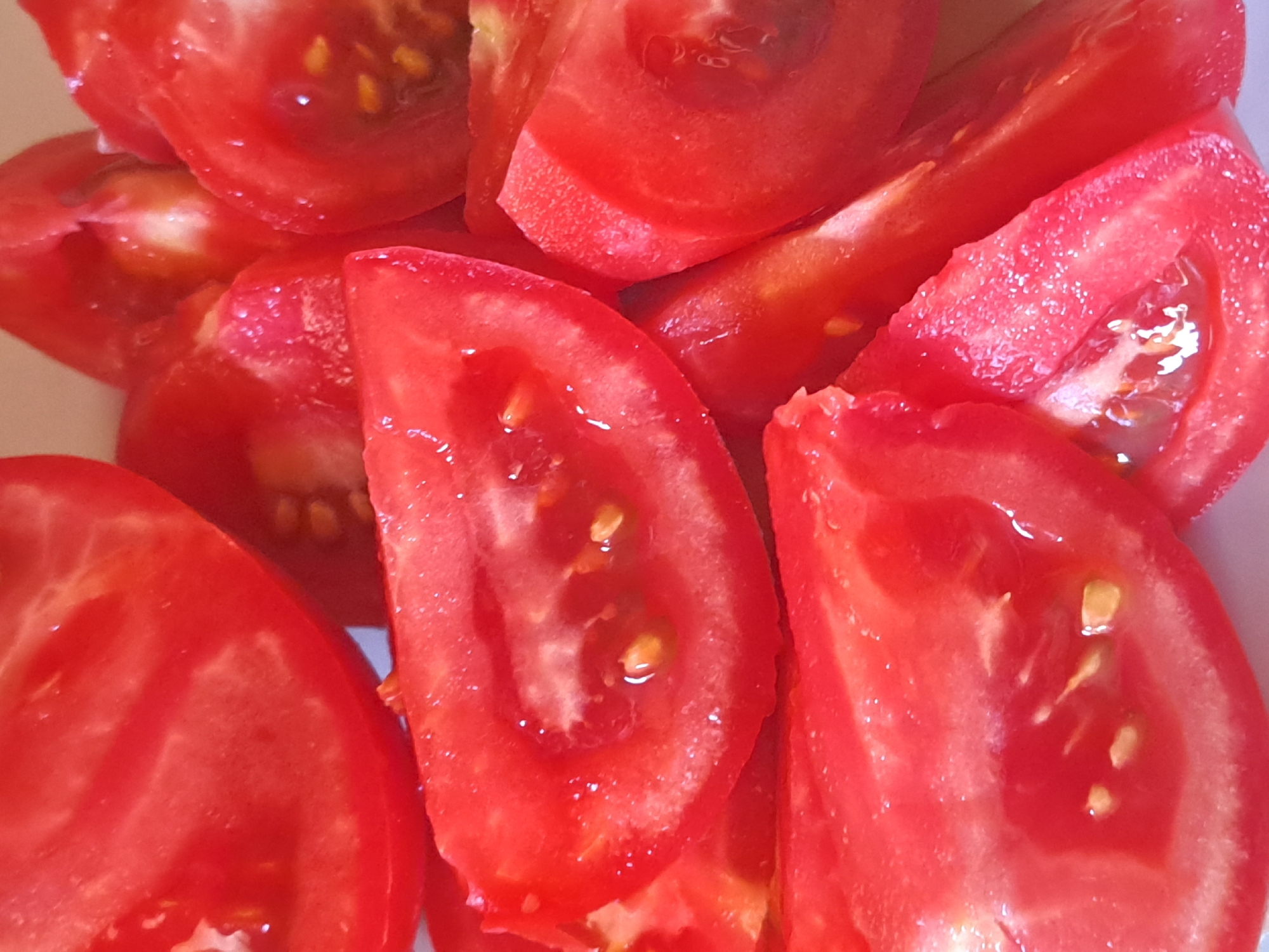 A close-up, overhead shot displays several sliced tomatoes on a white plate. The tomatoes are bright red and juicy, with visible seeds and pulp. Some slices are whole, while others are cut in half, revealing their inner structure. The lighting is bright, creating reflections on the wet surfaces of the fruit. The image is centered and focuses on the texture and color of the tomatoes. This scene is not specifically located in Vypasne, Ukraine; it is a generic depiction of sliced tomatoes.