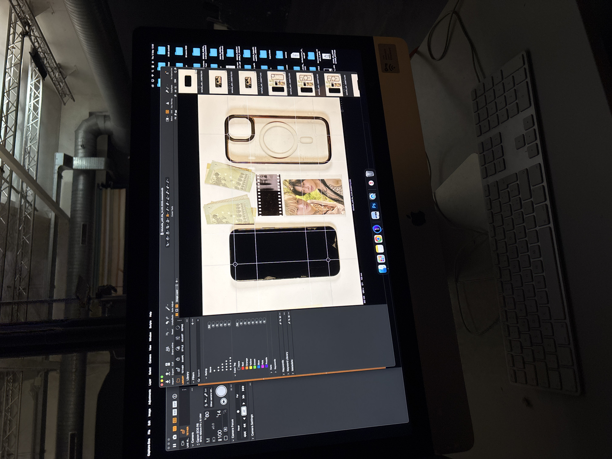 The image shows a digital workstation, likely used for photography or graphic design, indoors. On the large display, the Capture One software is open, showing a series of images depicting a phone case with some money and photographs. The software interface indicates a Canon EOS R6 camera is connected. To the right of the monitor, part of a white Apple keyboard and a mouse are visible. The background features an industrial interior with exposed structural elements, possibly a studio or warehouse-like space. The image does not specify a location in Milan, Italy.