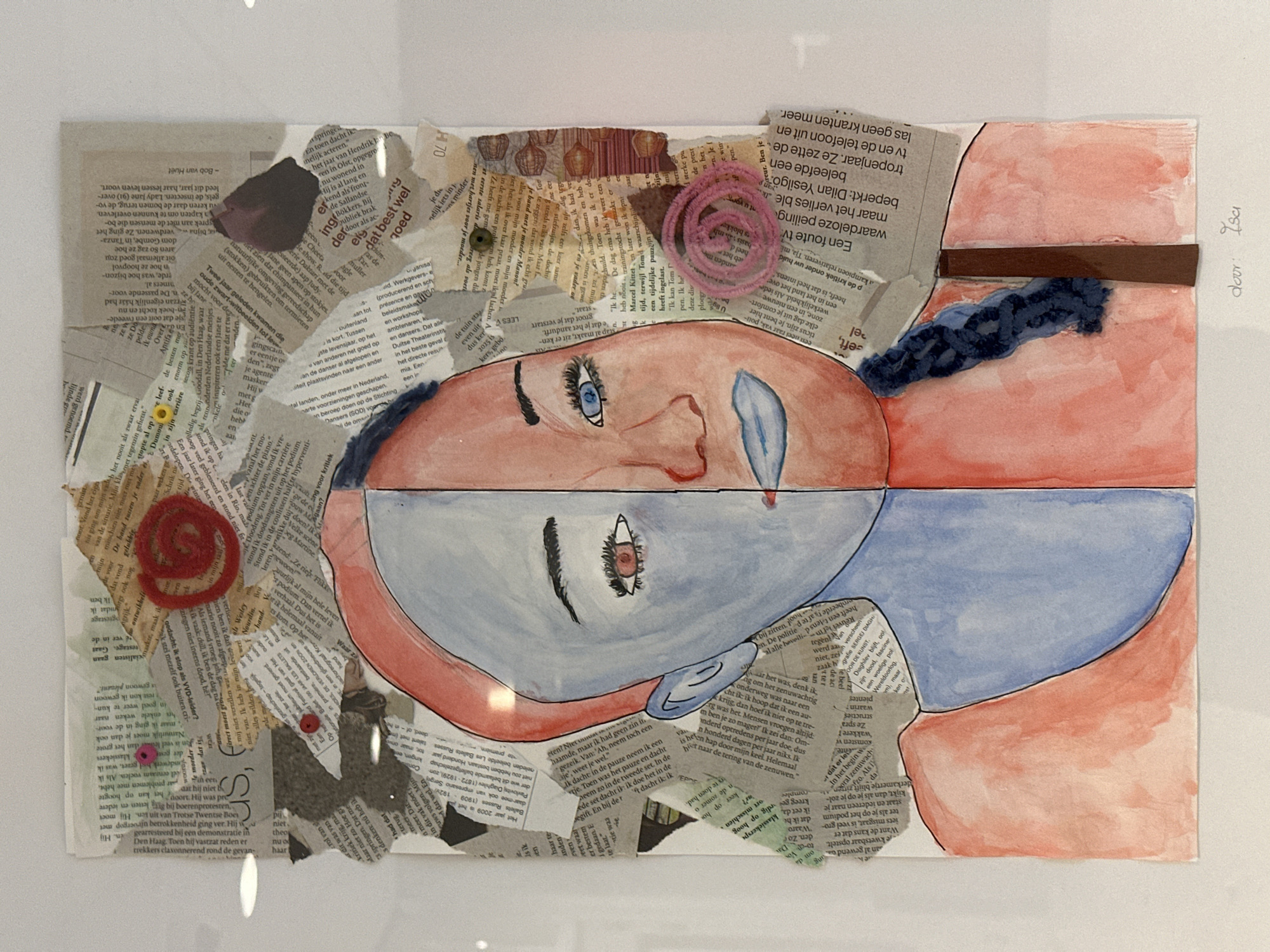 The image displays a mixed-media artwork, photographed indoors against a plain white background in Almelo, Netherlands. The central subject is a stylized human head, horizontally split into two distinct halves.
The top half of the face features reddish-pink skin tones, an open blue eye looking upwards, and a single blue teardrop falling from it. Dark, textured hair, possibly a braid or twist, is visible on the right side of the head, while other areas are covered by collage elements. The bottom half of the artwork presents an inverted image or reflection of the head, rendered in cool blue-grey skin tones, with a dark eye looking downwards, contrasting with the upward gaze of the top.
The artwork's background and parts of the face are constructed from a collage of torn newspaper clippings, predominantly featuring Dutch text. Various small embellishments are integrated into the collage: pink spiraled yarn is visible near the top right, red spiraled yarn on the bottom left, along with small yellow flower-like elements and a pink bead or sequin. A piece of brown paper or fabric spans horizontally across the right side of the artwork.
Visible text on the collage includes fragmented Dutch phrases like "Bob van Huel," "LEES," "twee jaar geleden kwamen die," and "Een foute tv." The artist's signature "door Isa" (by Isa) and the year "2020" are visible in the top right corner of the artwork. The composition suggests themes of duality, emotion, and introspection.