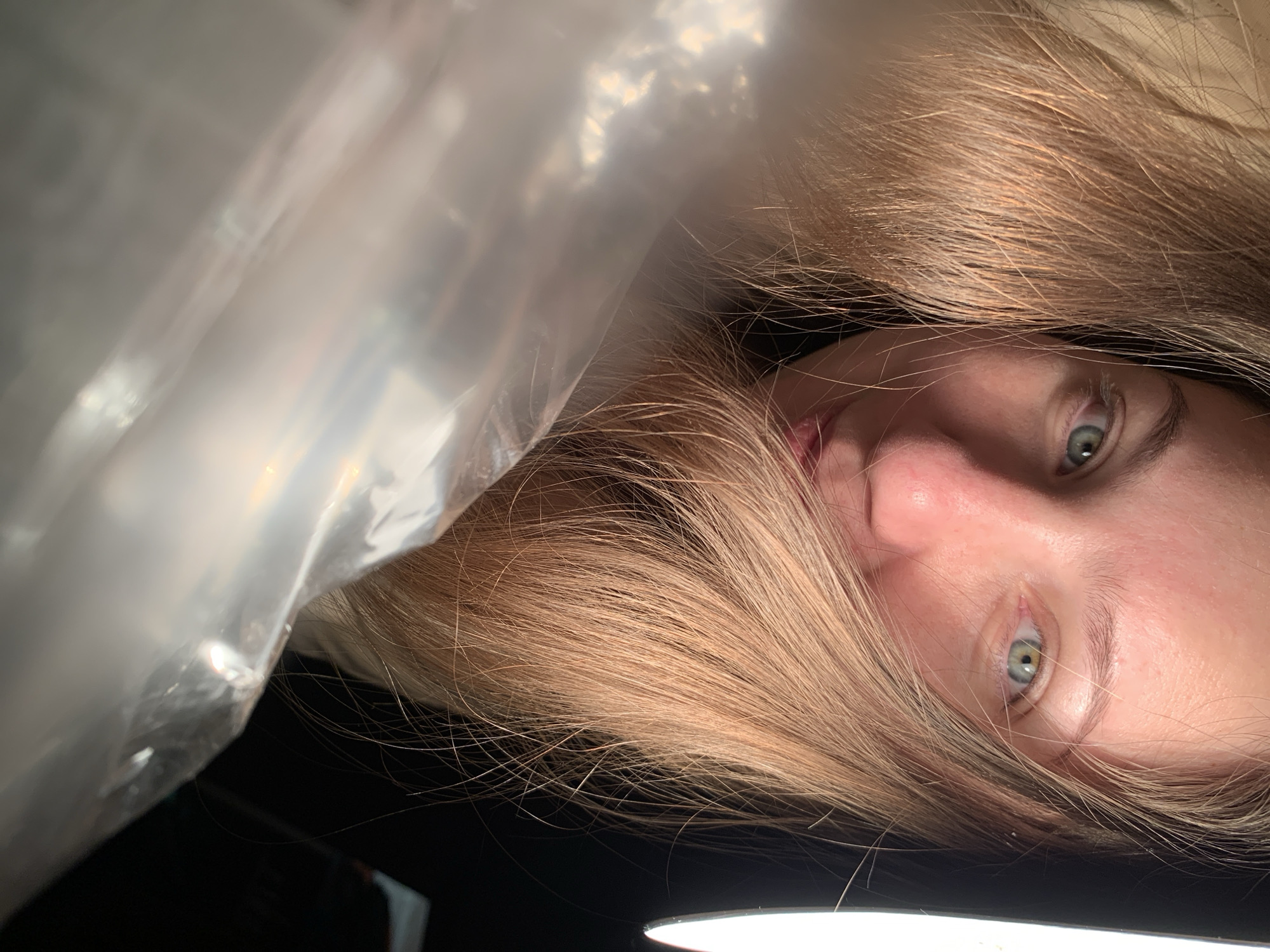 The image shows a person with light brown hair and light-colored eyes. A semi-transparent, plastic-like material is positioned above the person's face, partially obscuring the view. The background appears to be dark, and a light source is visible at the bottom of the frame. It is not possible to determine the location of the image as Chaikovsky, Russia, from visual information alone.