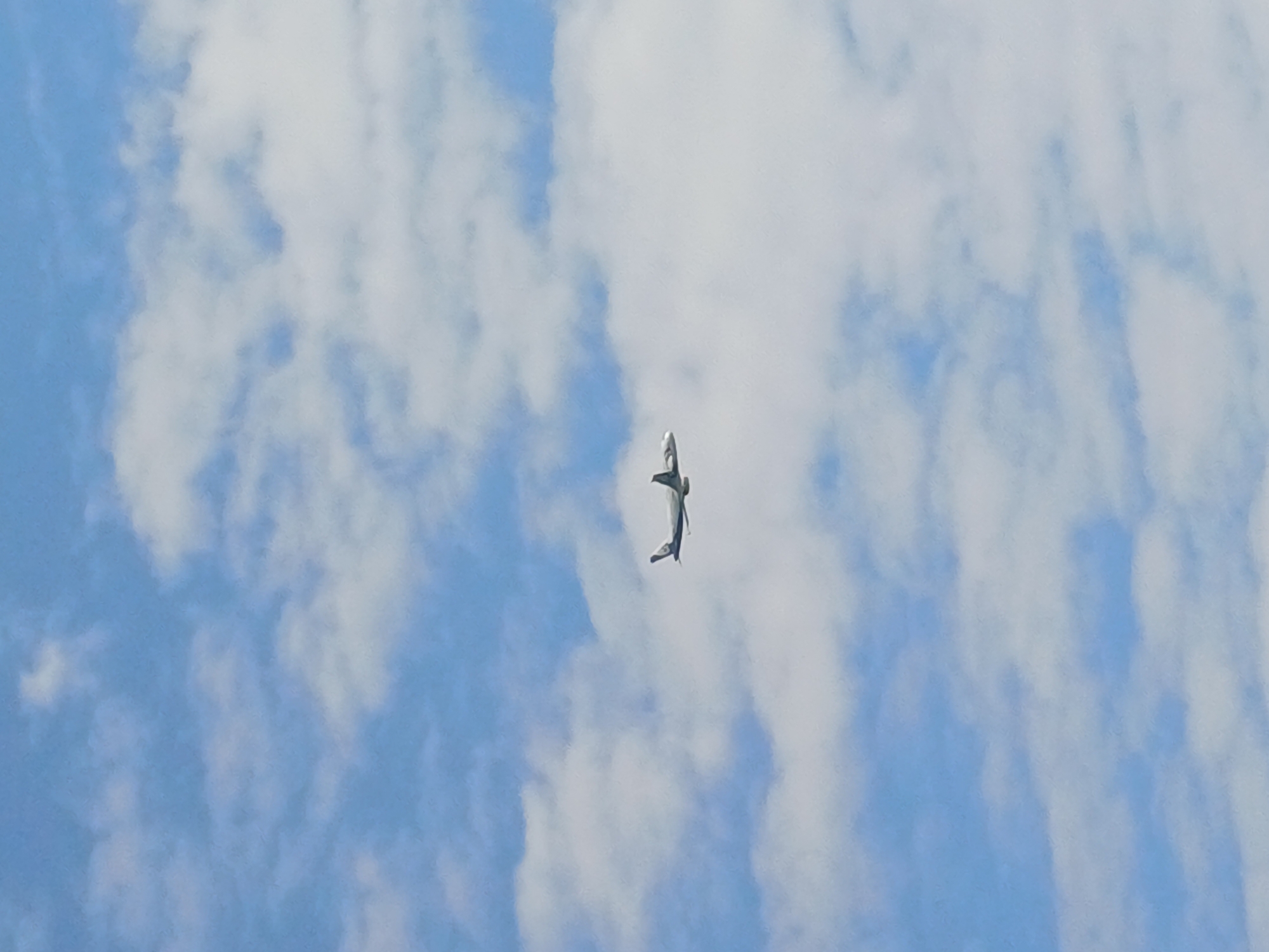 An airplane is visible in the sky, flying against a backdrop of clouds. The airplane is small in the frame, appearing as a distant object against the vast expanse of the sky. The clouds are white and fluffy, scattered across a light blue sky. The image does not contain any information that would allow for its placement within the city of Sochi, Russia, or any other specific geographical location. There are no people or other discernible objects or actions depicted in the image.