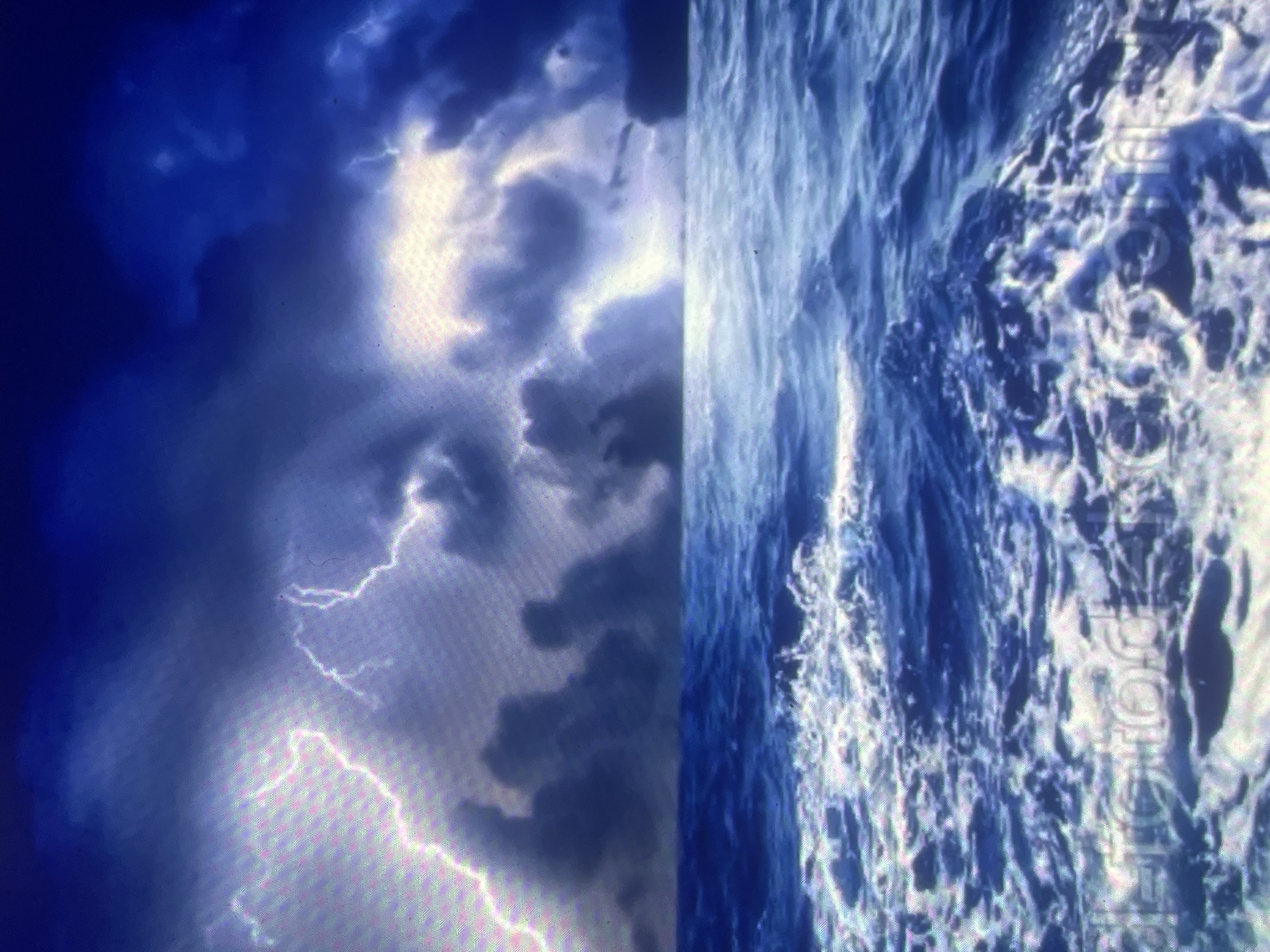 The image depicts a turbulent marine environment under a dark, stormy sky, with the scene purportedly located in the city of Zelenyi Hai, Ukraine. The upper half of the image features heavy, dark blue and gray storm clouds, actively illuminated by multiple prominent streaks of white and light purple lightning. These lightning strikes signify intense atmospheric electrical discharge. Patches of brighter light are visible breaking through or reflecting off the clouds in various sections, suggesting distant or obscured light sources behind the storm. The lower half of the image portrays a rough, dark blue sea characterized by numerous whitecaps and foamy waves in motion, filling the foreground and extending towards a distinct horizon line. The water shows dynamic movement, indicative of strong winds and rough conditions. No land features, vessels, people, or other specific objects are visible in the environmental scene. Faintly visible in the bottom section of the image is a watermark or text, "detorodka.com.ua".