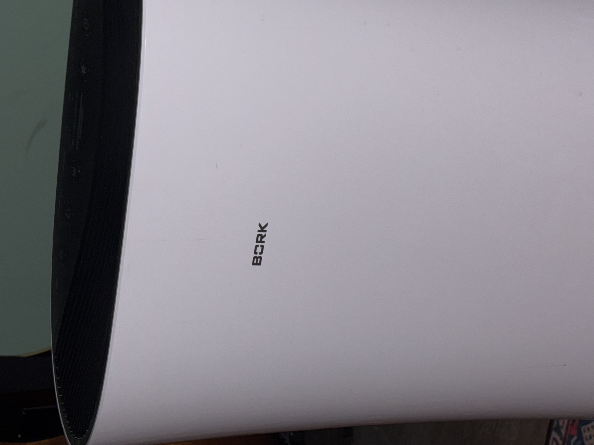 The image shows a close-up view of a white appliance, likely an air purifier, with the brand name "BORK" printed in black letters on its surface. The top of the appliance features a black, ribbed section with some visible control buttons. The background is blurred, but appears to be an indoor setting with a greenish wall and a glimpse of a wooden surface. The overall impression is a static shot of a household appliance. There is no information in the image that places it in Yuzhno-Sakhalinsk, Russia.