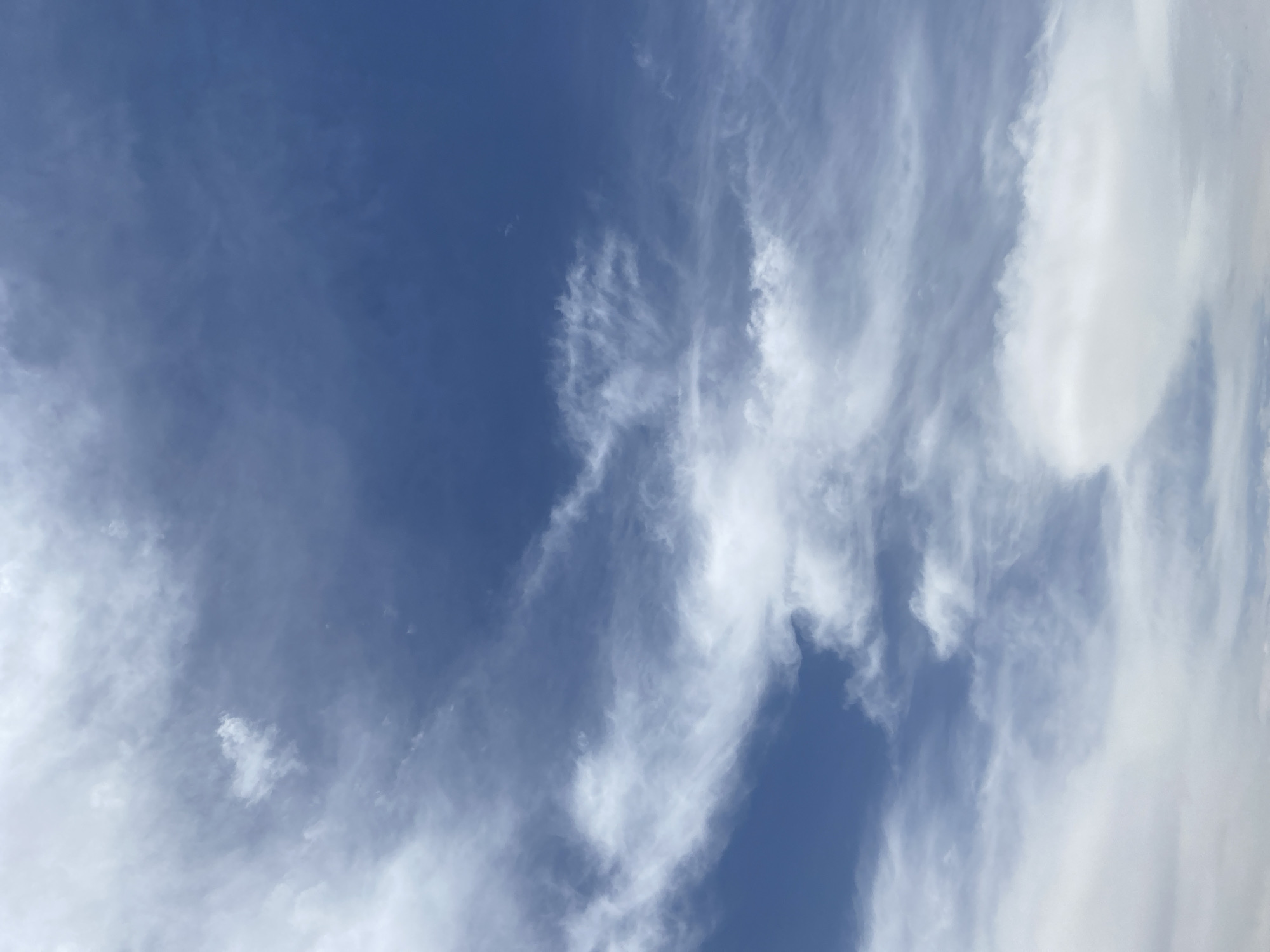The image depicts a blue sky with wispy white clouds. No evidence suggests this image was taken in Rido, Nigeria. No people or objects are visible. The only action is the movement of clouds. The environment is a daytime sky.