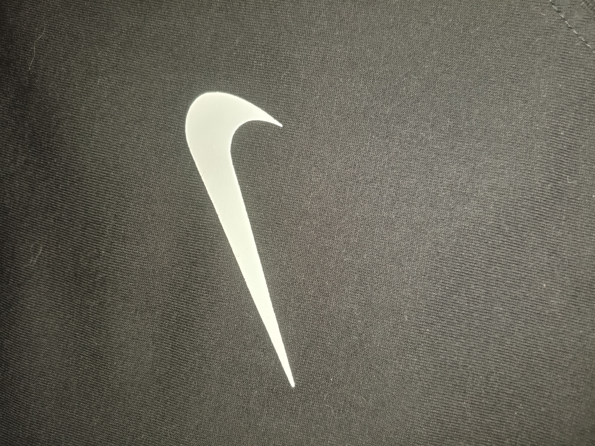 A white Nike swoosh logo is prominently displayed on a dark gray or black textile fabric. The fabric appears to have a ribbed or woven texture. The background is uniform in color and texture. The location in Puchezh, Russia is not evident from the image. There are no people or actions visible in the image.