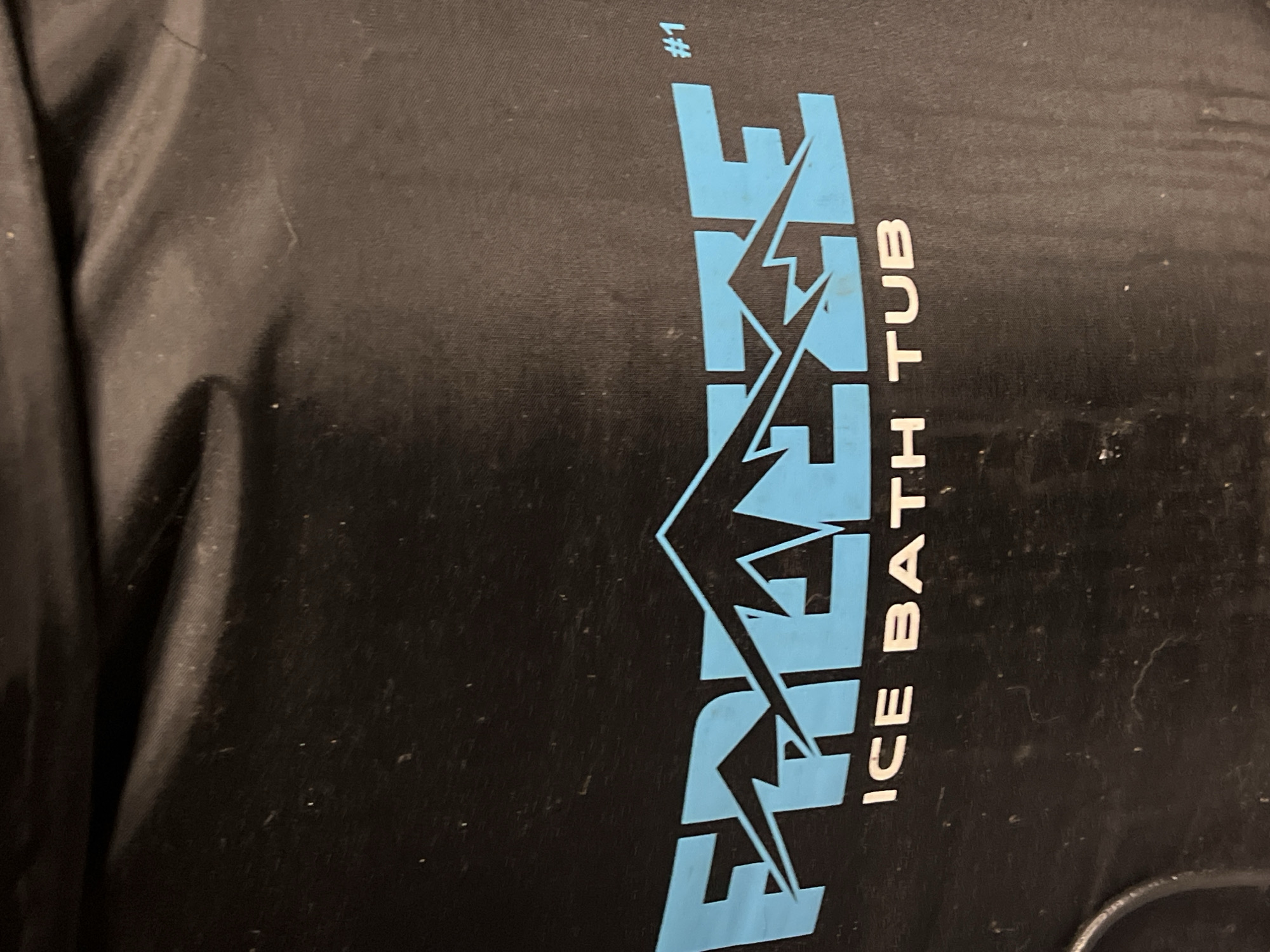 The image shows a close-up of a black material with light blue lettering that reads "FREEZE ICE BATH TUB #1". The material appears slightly wrinkled and may be part of a larger product. The city of City of Newburgh and country United States of America cannot be determined from the image content.