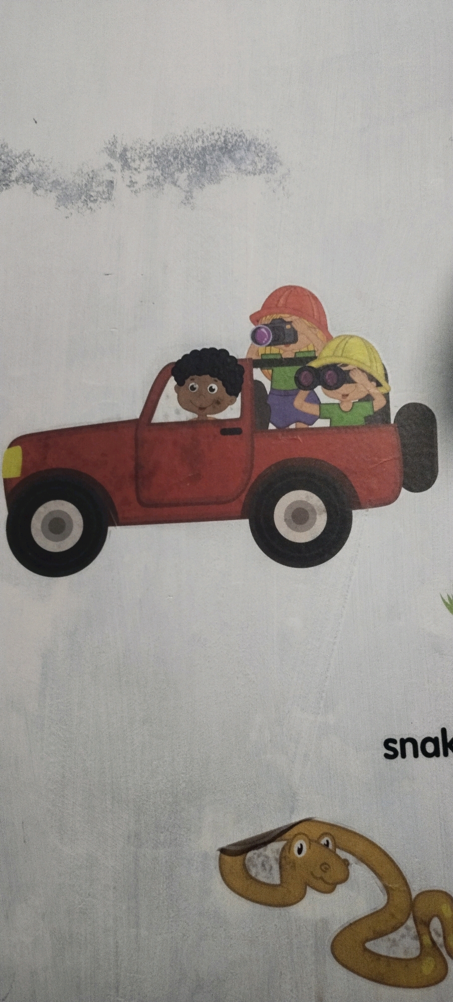 The image depicts a cartoon illustration on a light-colored, textured background. In the upper portion of the image, a red toy truck carries three cartoon characters. The driver, a child with dark curly hair, is in the front seat. Two children are in the back, both wearing hats and looking through binoculars. One child wears an orange hat and has a camera around their neck. The other child wears a yellow hat. Below the truck, a cartoon snake with yellow and brown markings is coiled. To the right of the snake, the word "snake" is printed in black, sans-serif font. There are no discernible elements related to the city of Daleman, Indonesia.