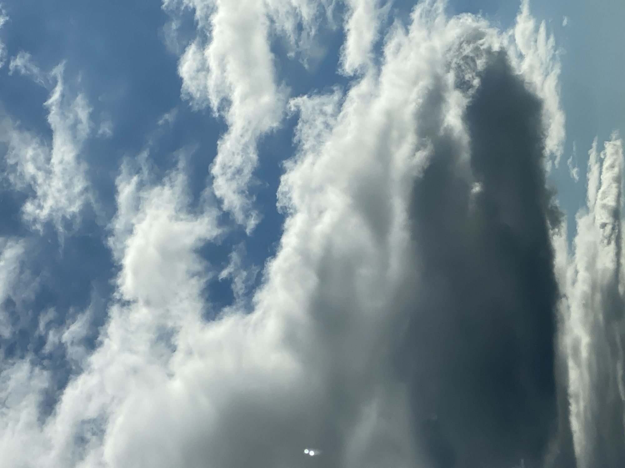 The image shows a cloudy sky with blue patches visible. There are several large, white, and grey clouds of varying density. Some smaller, wispy clouds are also present. In the lower left portion of the image, there are two small, bright, circular light reflections. The sky appears to be a clear day with scattered clouds, suggesting good weather conditions. There are no visible landmarks or structures indicating a specific city or location, therefore, the location in Berga, Germany cannot be confirmed.
