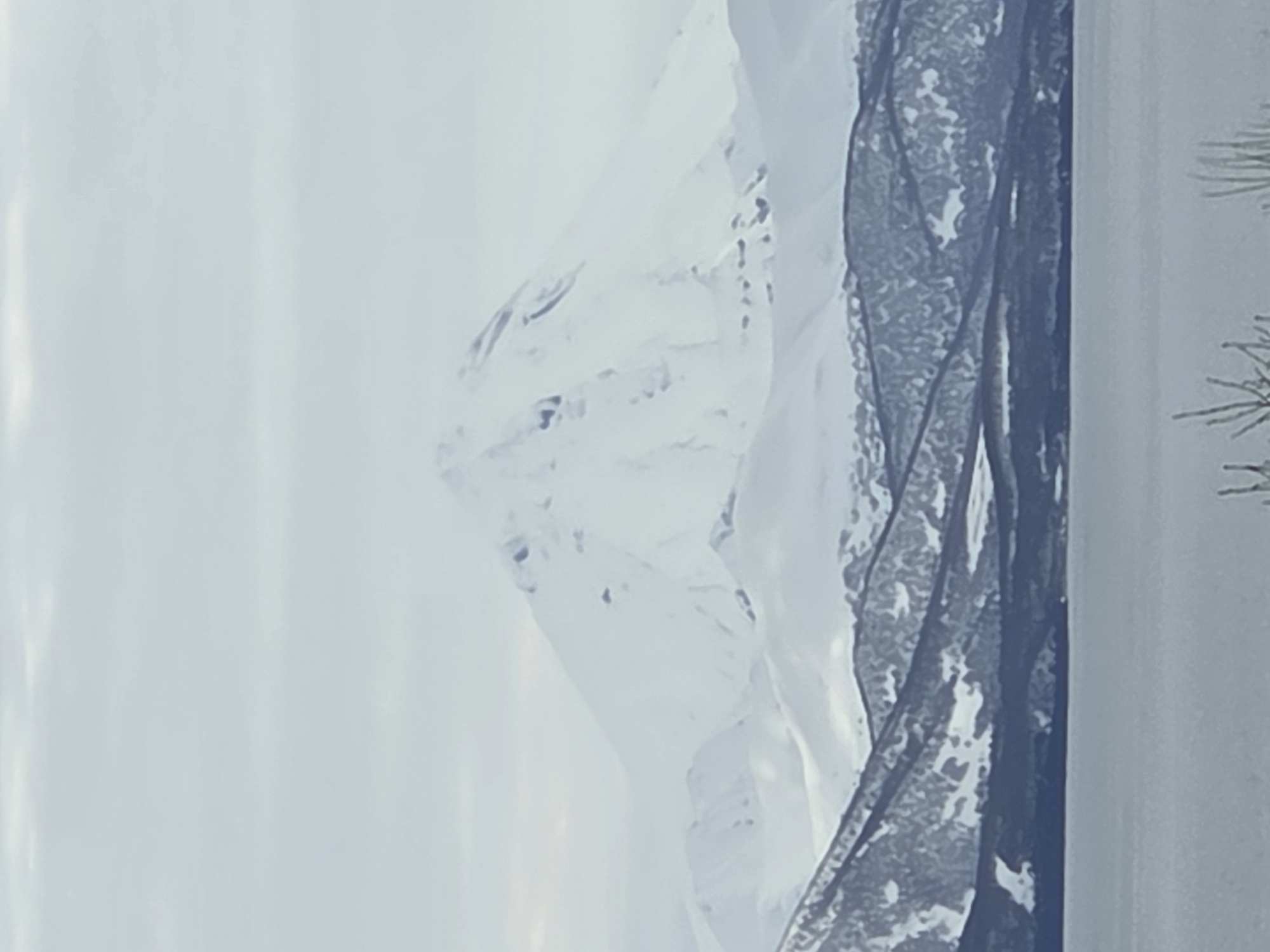 The image shows a snowy mountain range, viewed through a window obscured by a dark, possibly frozen or icy, pattern. The location is Unknown, Unknown. The environment is cold and snowy.