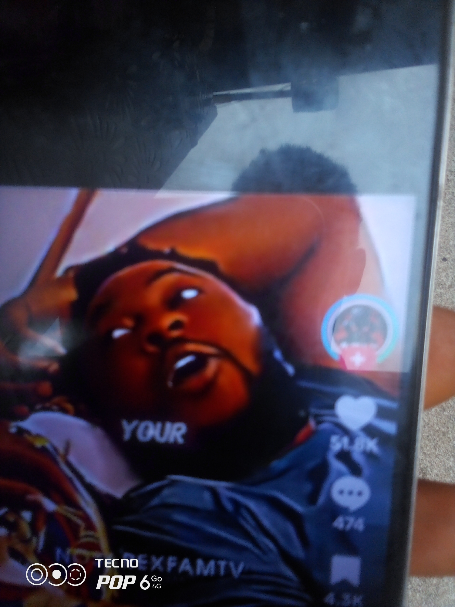 The image is a photograph of a smartphone screen displaying a video. The video appears to be a short-form clip, possibly from a social media platform like TikTok or Instagram, given the icons for likes, comments, and shares visible on the right side of the screen. The video content itself shows a person's face from a close-up, angled perspective. The person has dark skin and is looking upwards with their mouth slightly open. The lighting is somewhat harsh, creating bright reflections in their eyes. Text overlays are visible on the screen, with "YOUR" appearing in large white letters on the left. At the bottom of the screen, there is branding for "TECNO POP 6 Go 4G", indicating the device model. The background of the video is blurred and appears to be a dark-colored garment or fabric. The phone itself is held by a hand, part of which is visible on the right edge of the frame, suggesting the image was taken by someone holding the phone. There are no discernible elements in the image that would allow for the identification of a specific location in Howayi, Nigeria, or any other city. The image focuses entirely on the content displayed on the smartphone screen and the device itself.