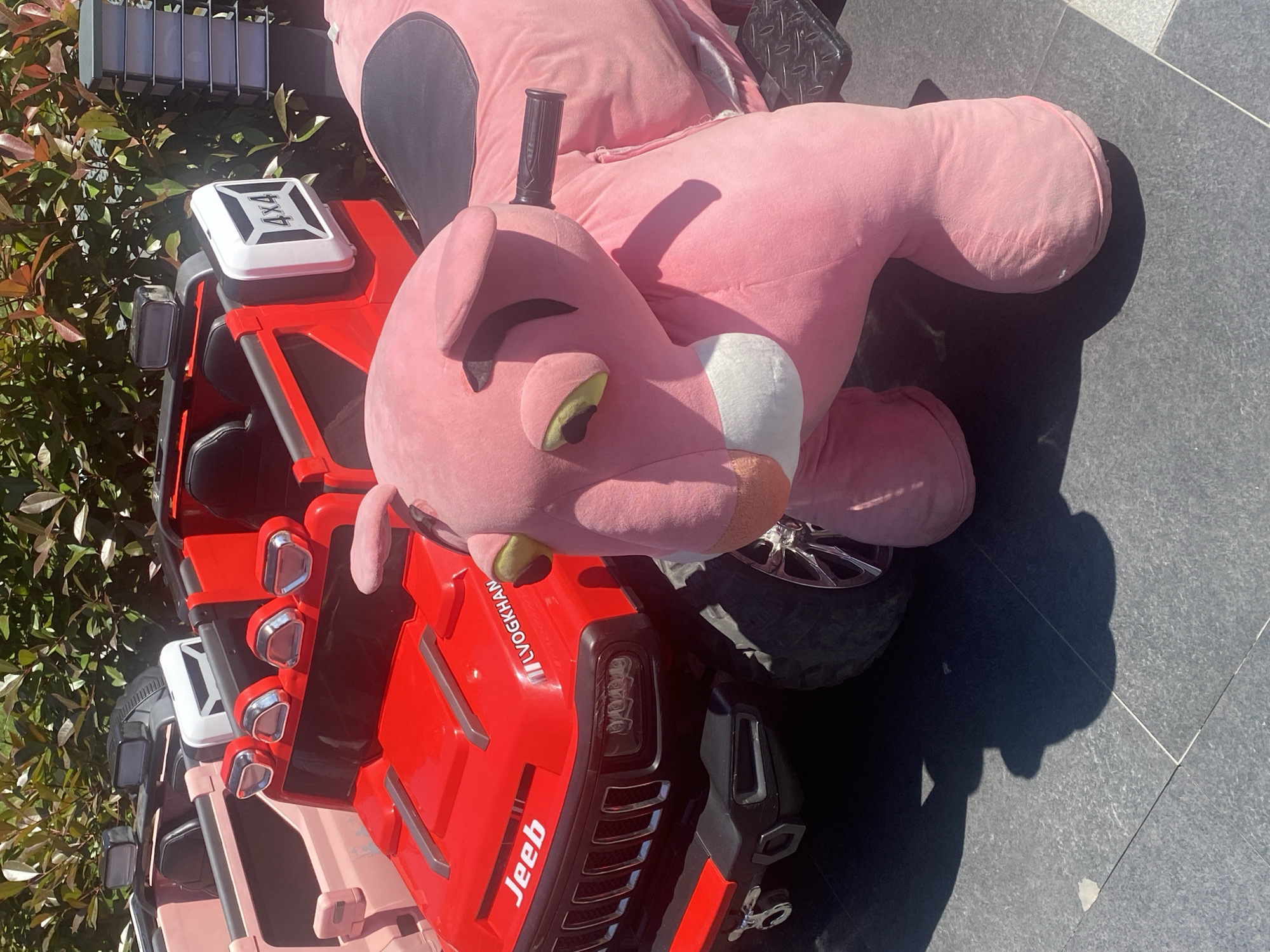 A large pink plush panther toy lies on a red toy Jeep. The Jeep has a "JeeB" label and "LVOGKHAN" markings. The setting appears to be outdoors on a tiled surface, possibly in a public area. The photo was taken in Çekmeköy, Turkey.