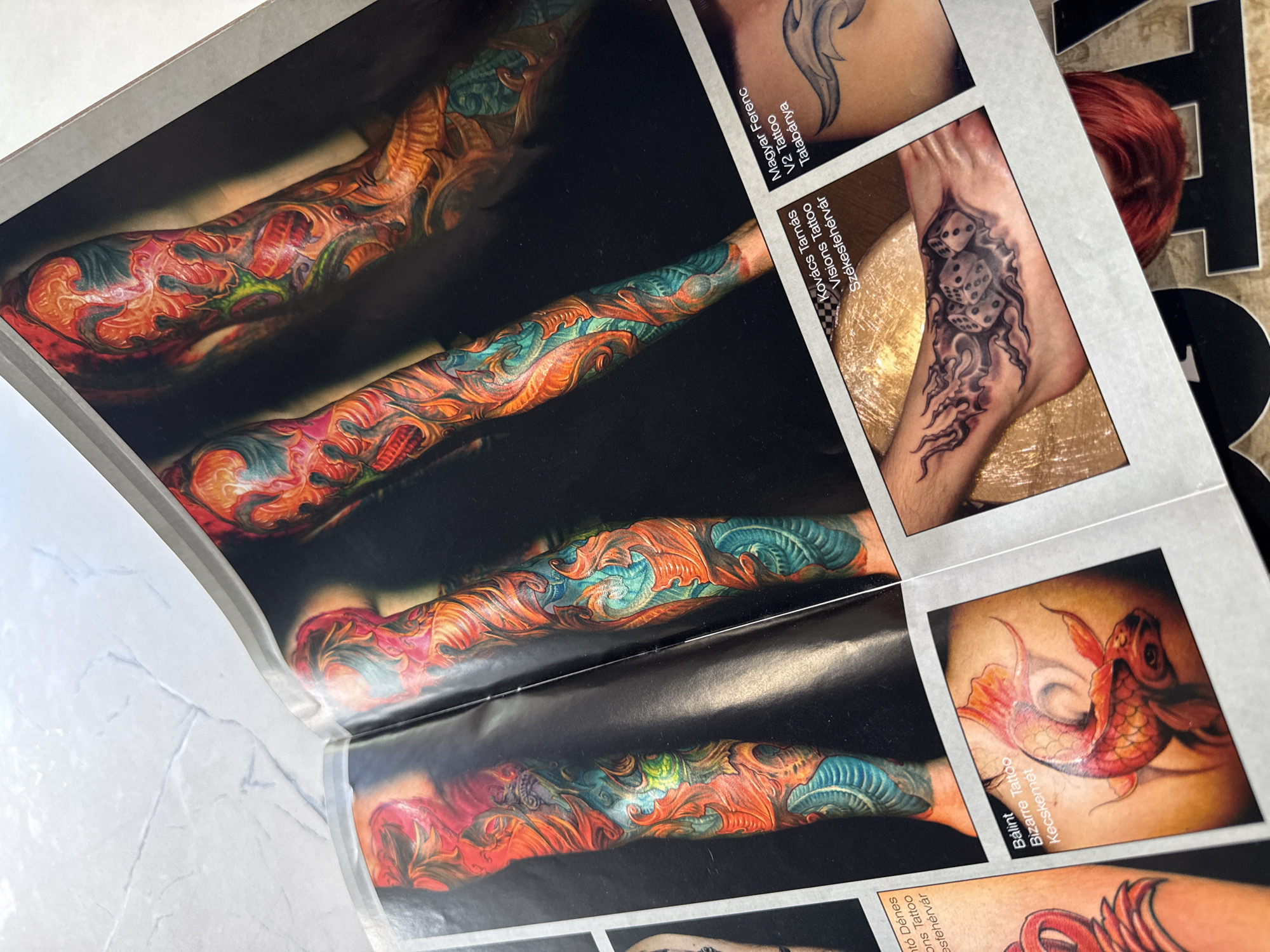 The image shows a spread from a tattoo magazine or portfolio. The spread features close-up photographs of various tattoos on different body parts. The tattoos displayed include a full arm sleeve with an organic, abstract design in orange, teal, and red hues, a foot tattoo of dice and tentacles, and a koi fish tattoo. Text accompanying each image indicates the tattoo artist's name, studio, and city within Hungary, specifically Tatabánya, Székesfehérvár, and Kecskemét. The background is not visible in the image. There is no evidence to indicate that this scene is located in Sofia, Bulgaria.