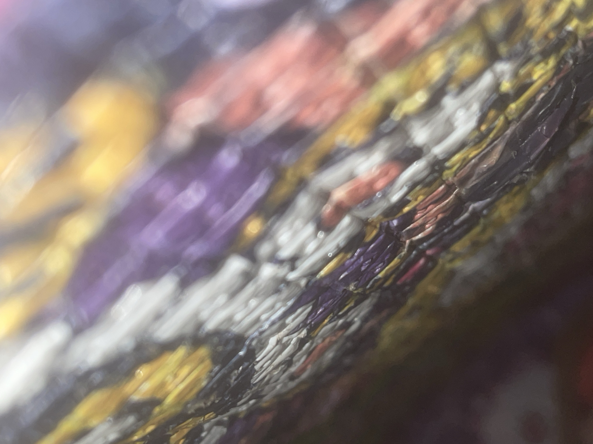The image is a close-up, macro shot of a woven textile or material. The texture is rough and appears to be made of numerous thin strands or fibers interlaced diagonally. The colors are vibrant and include purple, white, yellow, and shades of pink and red. The focus is shallow, with some areas blurred, creating a sense of depth and highlighting the intricate details of the weave. The lighting appears to be artificial, casting a slight sheen on some of the fibers. There is no discernible urban or natural environment, people, or specific location within Howayi, Nigeria, visible in this abstract close-up of the material.