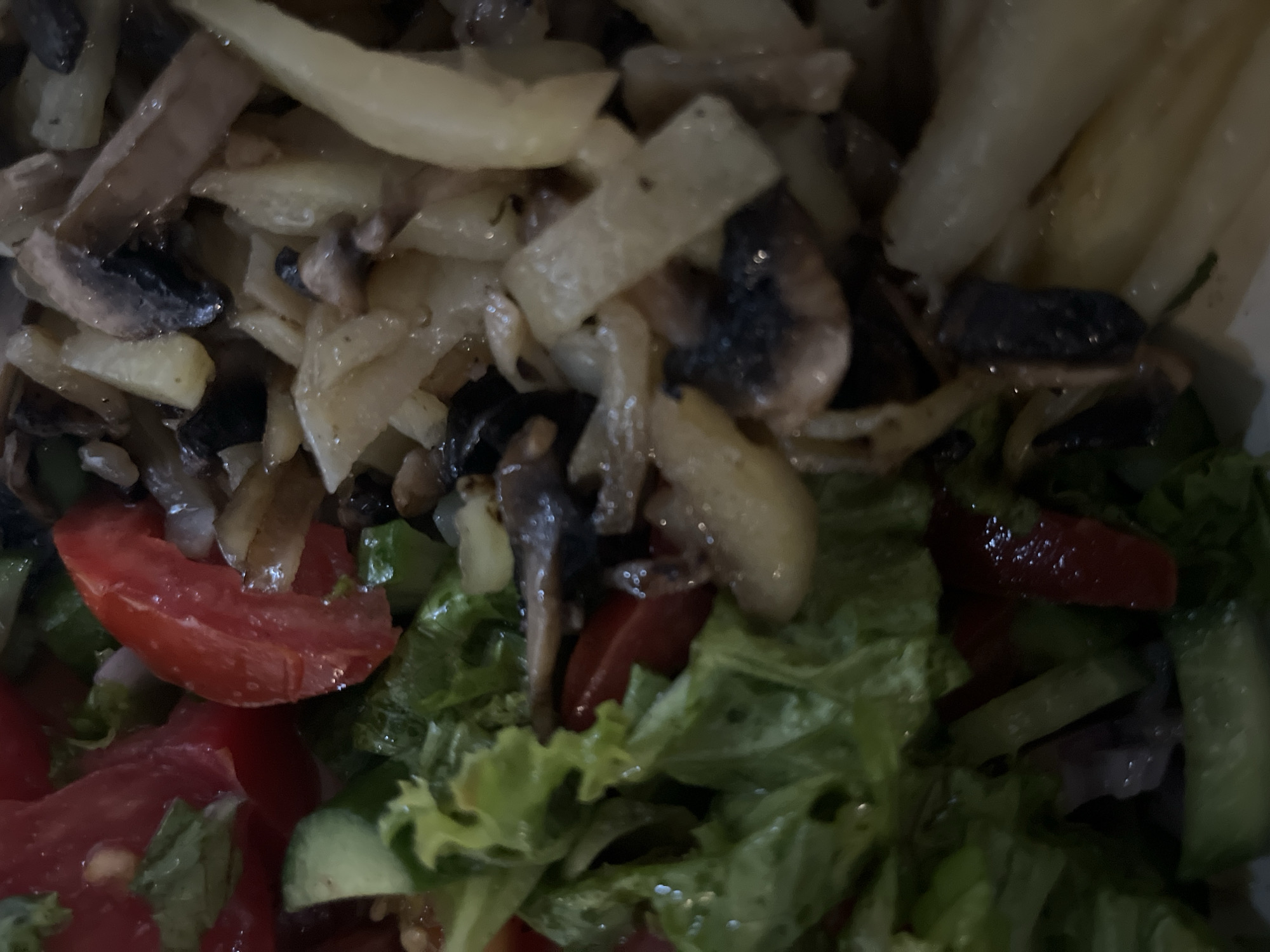 The image shows a close-up of a salad consisting of sauteed vegetables on top of fresh vegetables. The sauteed portion includes mushrooms and elongated white/yellow pieces resembling potatoes or onions. The fresh vegetable component contains lettuce, sliced tomatoes, and sliced cucumbers. The location and city of Unknown, Indonesia is not discernible from the provided image.