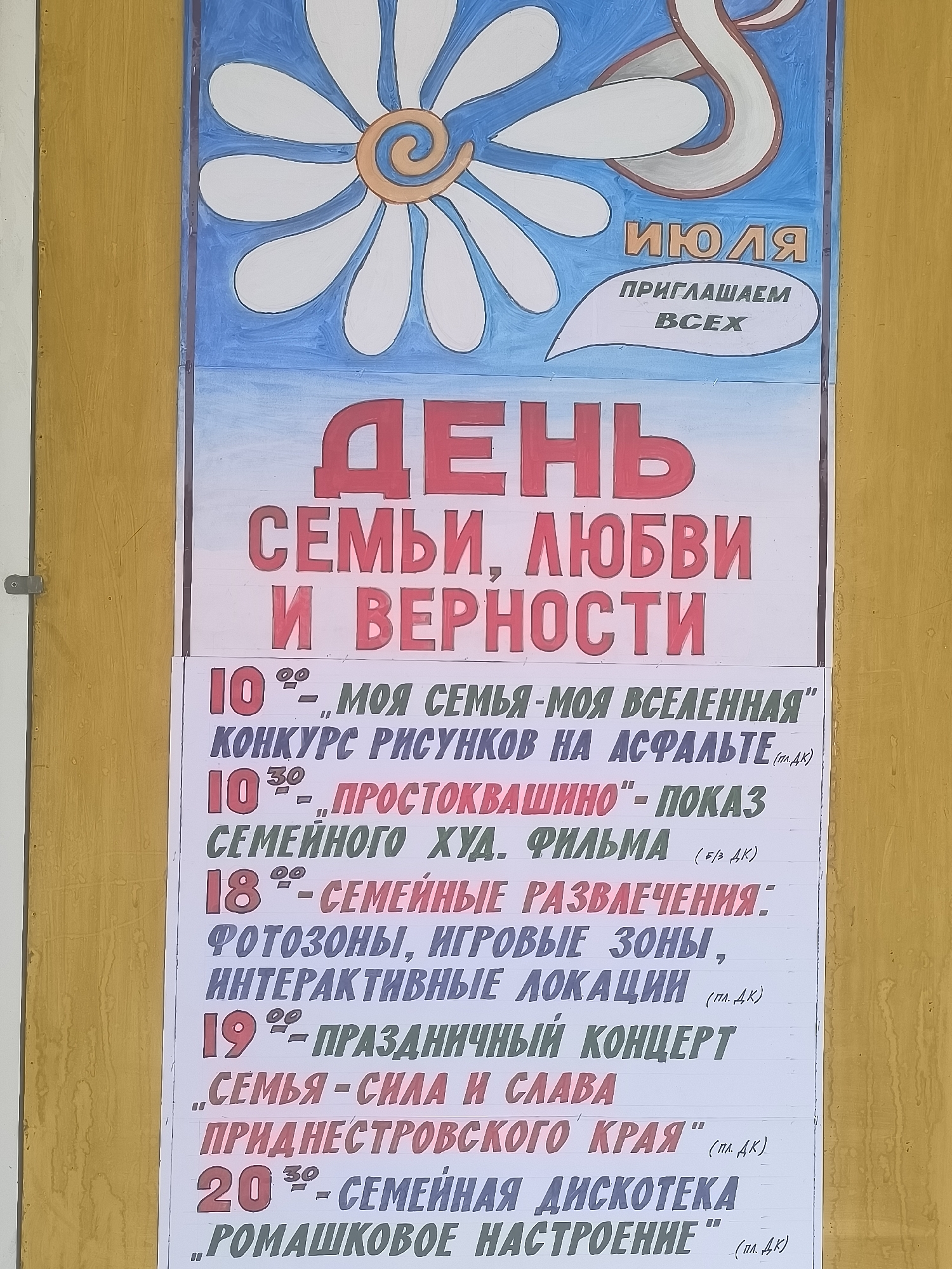 The image shows a poster on a yellow wall, likely in Tiraspol City Council, Moldova. The poster features a large daisy graphic at the top and colorful text announcing events. The main heading in large red letters reads "ДЕНЬ СЕМЬИ, ЛЮБВИ И ВЕРНОСТИ" (Day of Family, Love and Fidelity). Below this, a list of events with dates and times is presented. These include a drawing contest on asphalt on July 10th at 10:00, a film screening on July 10th at 10:30, and family entertainment with photo zones, game areas, and interactive locations on July 18th. On July 19th, there's a concert titled "Family is Strength and Glory," and on July 20th at 20:30, a family disco with the theme "Daisy Mood" is scheduled. The text is handwritten in Russian.