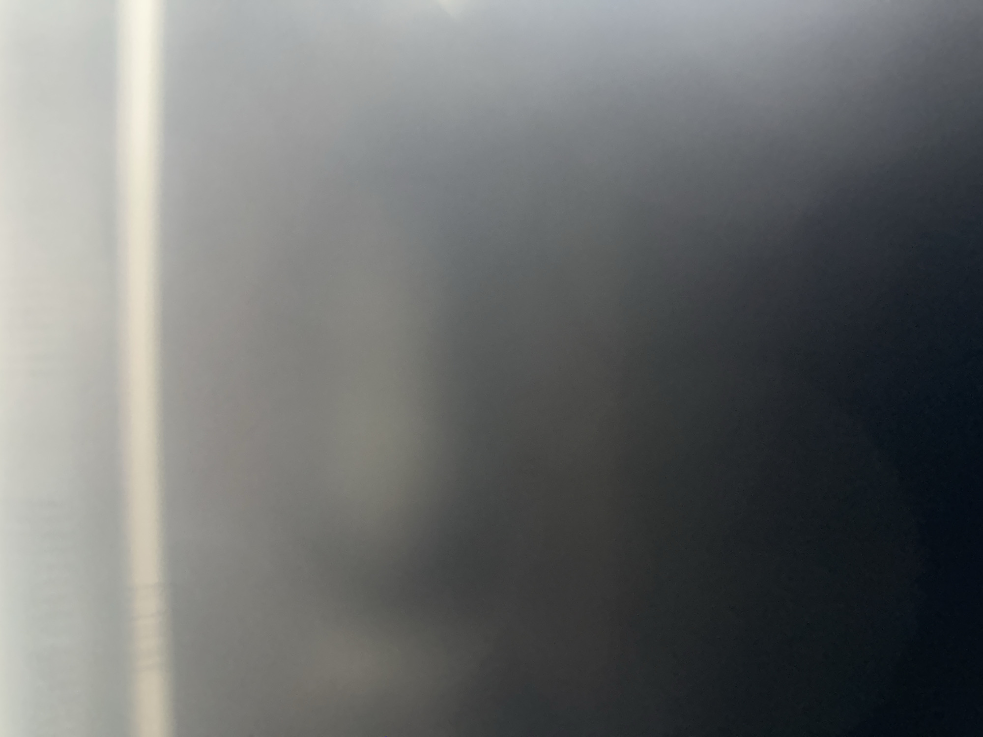 This is a close-up, abstract, and dimly lit media file. The primary subject appears to be a vertical, bright light source or reflection on the left side of the frame, casting a gradient of light across a dark, textured surface. This surface transitions from a lighter, diffused grey on the left to a deep, almost black hue on the right. There is a subtle, almost hazy form visible within the lighter grey area, which could be an indistinct object or a shadow. The lighting suggests an indoor setting, possibly with a single, strong light source off-camera or a strong reflection. The overall mood is somber and mysterious due to the low light and lack of clear subject matter. There is no visible text or discernible activity. The location context of Belgrade, Serbia, does not provide any direct visual cues within the abstract imagery.