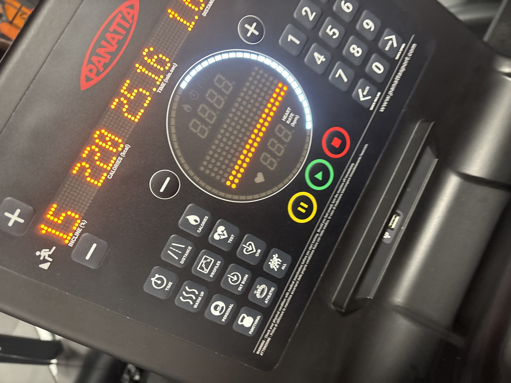 The image shows the control panel of a "Panatta" treadmill. The panel displays the following information: incline at 15%, calories burned at 220 kcal, and time elapsed at 25 minutes and 16 seconds. Other buttons on the panel include distance, calories, profiles, test, personal, fat burn, functional, athletic, warm up, and program buttons, as well as buttons to increase or decrease the incline, start, stop and pause buttons, and a number keypad.
There is no information about Plovdiv, Bulgaria, or a city in the image. There are no people visible in the image.