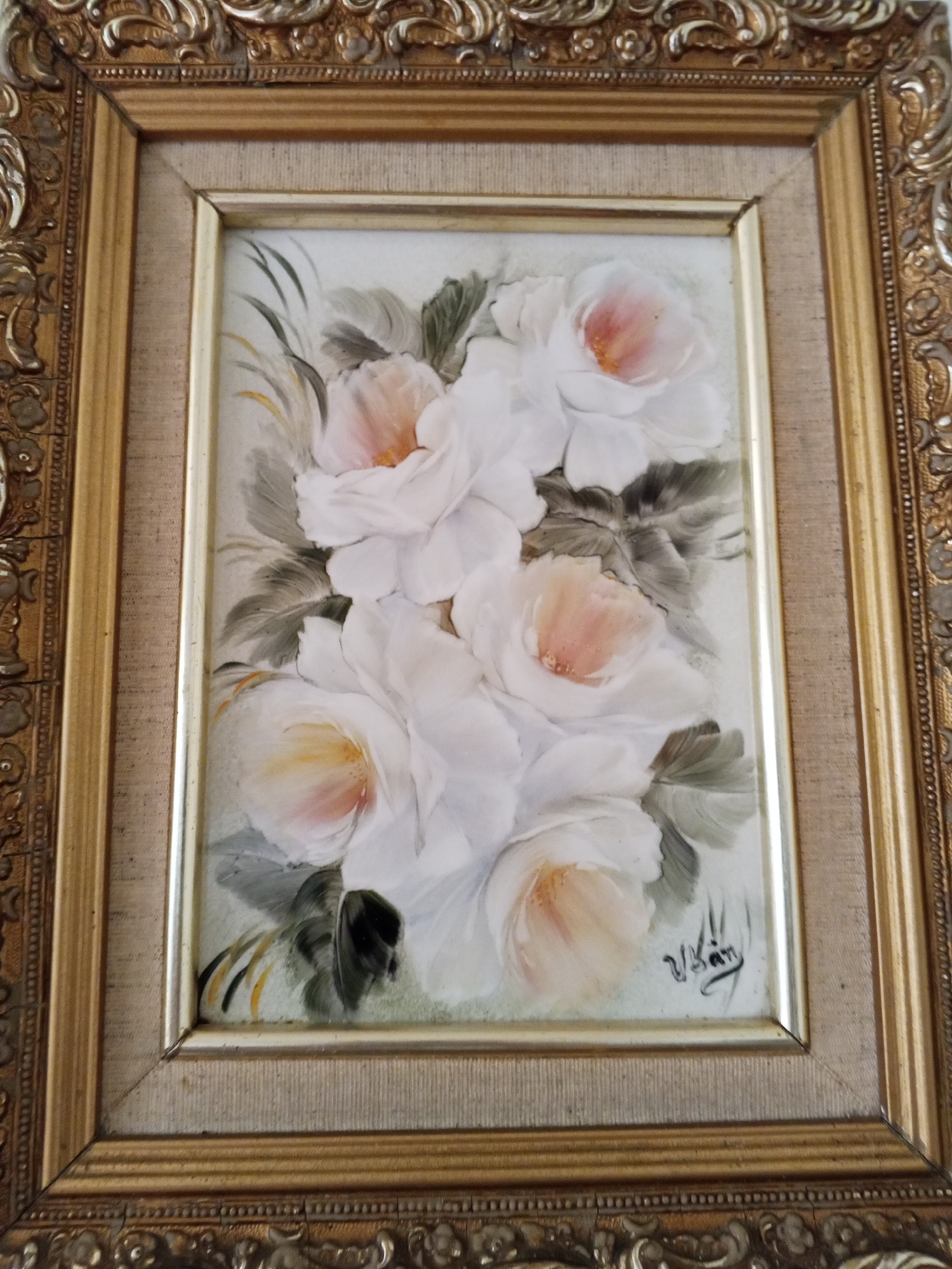 A framed painting of white and light pink roses is depicted. The frame is ornate with gold detailing. The painting has a signature in the lower right corner. The location is Tinaquillo, Venezuela, although this detail is not discernable in the picture alone.