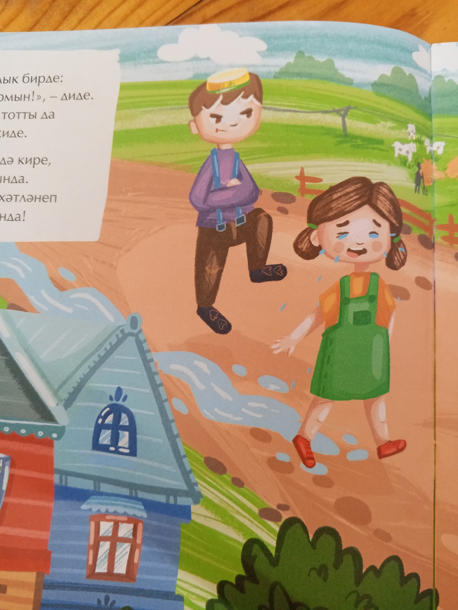 An illustration depicts a scene with two children in a rural setting. On the left, a boy with a stern expression and a yellow cap stands with his arms crossed. He wears a purple shirt with suspenders and brown pants. Beside him, a girl is crying, with tears streaming down her face. She wears an orange shirt and a green jumper dress, with red shoes. Puddles of water are scattered around them. In the background, a green field with a fence and scattered cows suggests a farm or countryside. To the left of the children, a stylized image of a house with red and blue sections is shown, with water flowing around it. The text on the left side of the image appears to be in a Cyrillic script. The overall scene appears to be from a children's book or story, with a whimsical and colorful artistic style. There is no visual information in the image that indicates a connection to the city of Chistopol, Russia.