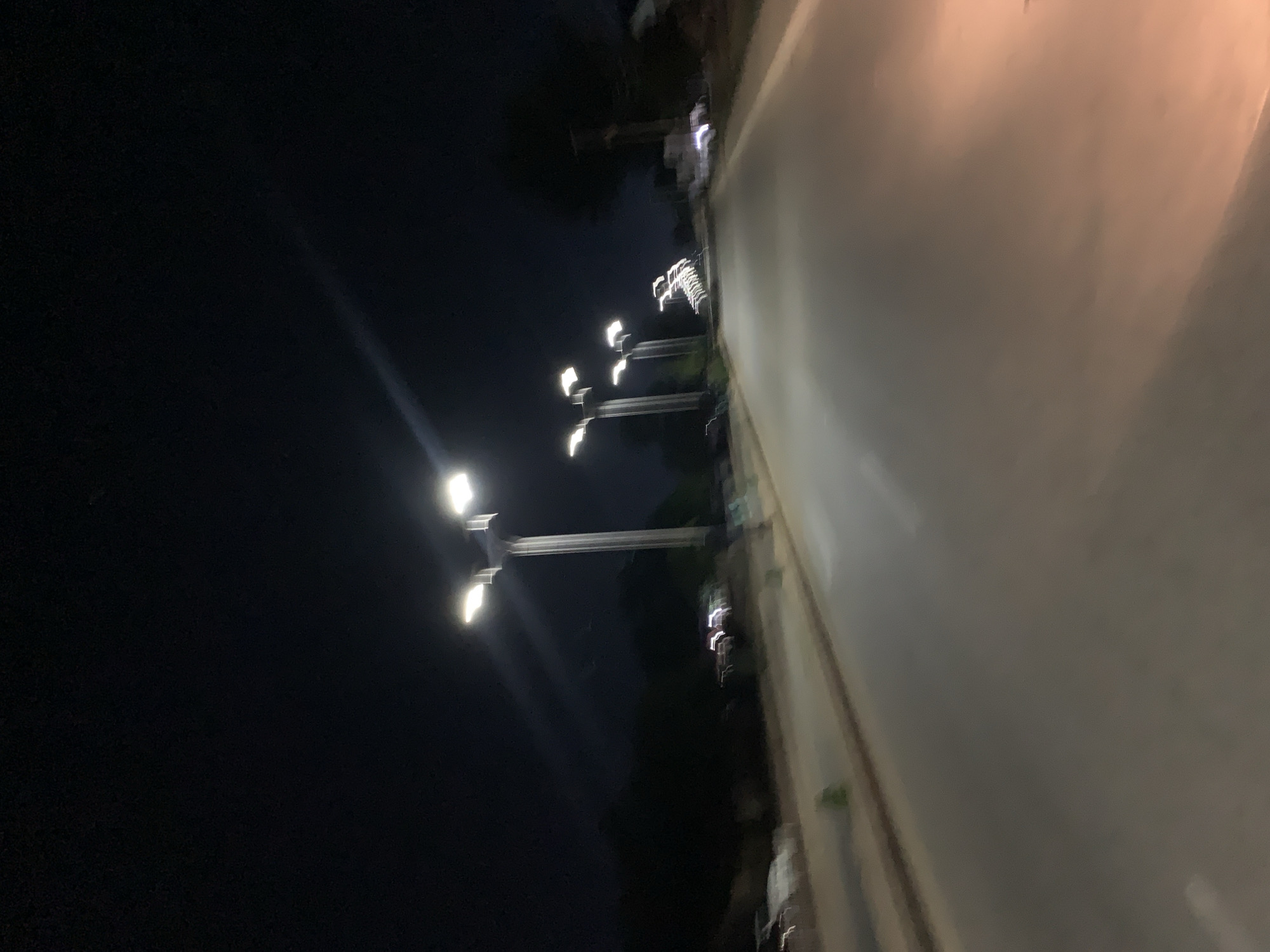 A poorly lit street scene at night, possibly in Kabong, Nigeria. There is a paved road with a row of streetlights along one side. The sky is dark. Some trees are present.