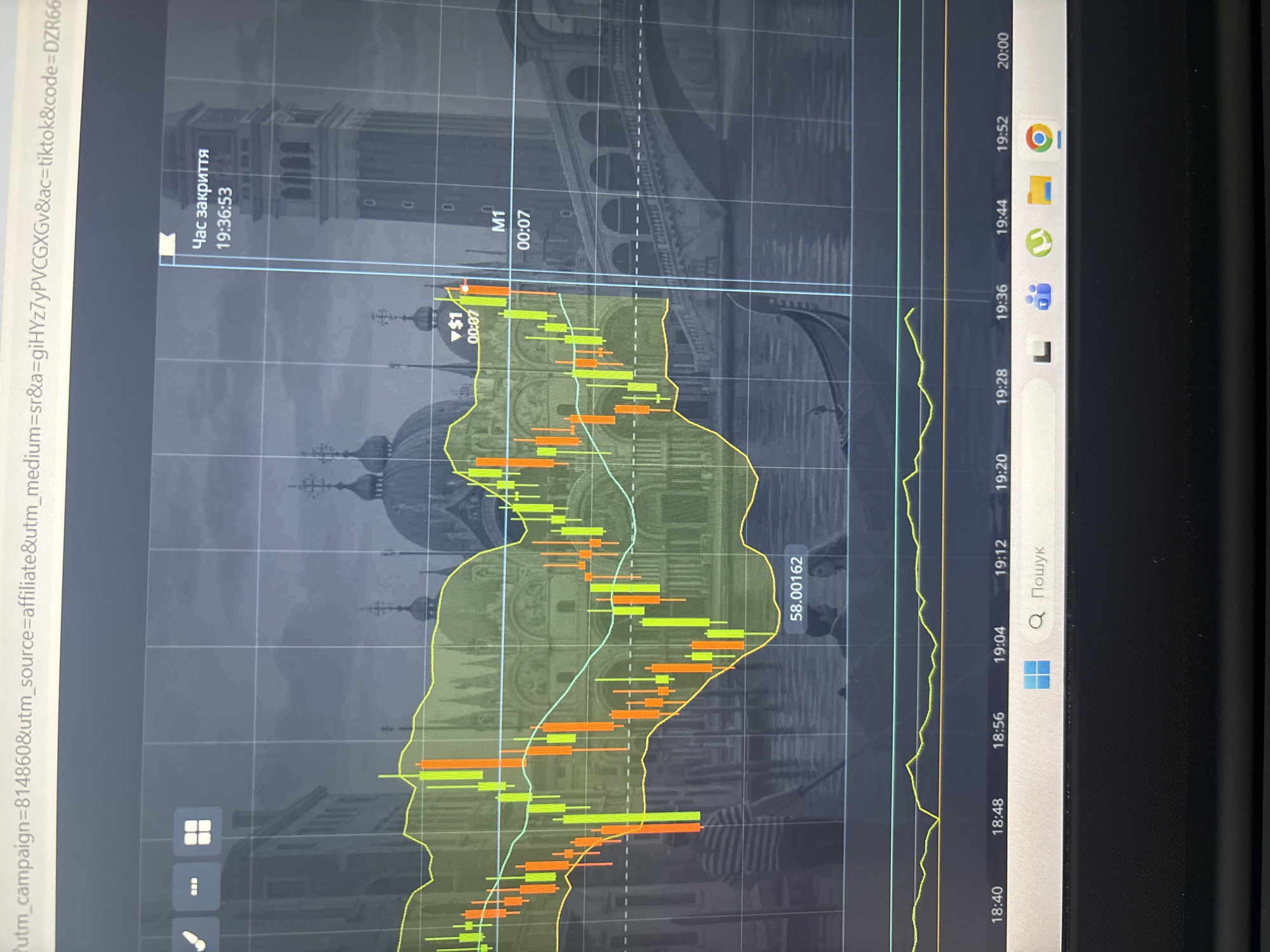 The media file displays a screenshot of a trading platform with a chart overlaid on an image of Venice, Italy. The chart shows candlesticks in green and orange, indicating price movements, with yellow and light blue lines representing technical indicators. The background image features gondolas and historic Venetian architecture, suggesting a romantic or scenic setting.
On the left side of the screen, a timestamp "19:36:53" is visible, along with the text "Час закриття" (Closing time). The chart itself has time markers along the bottom axis, ranging from "18:40" to "20:00". There is also a price marker "58.00162" visible.
In the top left corner, a URL is partially visible, containing campaign and source information.
The bottom right portion of the screenshot shows the Windows taskbar with icons for Google Chrome, File Explorer, Microsoft Teams, and other applications. A search bar is also present with the text "Q Пошук" (Search).
The overall impression is a digital interface, likely for financial trading, with a thematic background. The time indicated is evening. There are no people or discernible weather conditions depicted. The location context provided (Kalisz, Poland) does not seem to be represented in the visible content of the image itself.