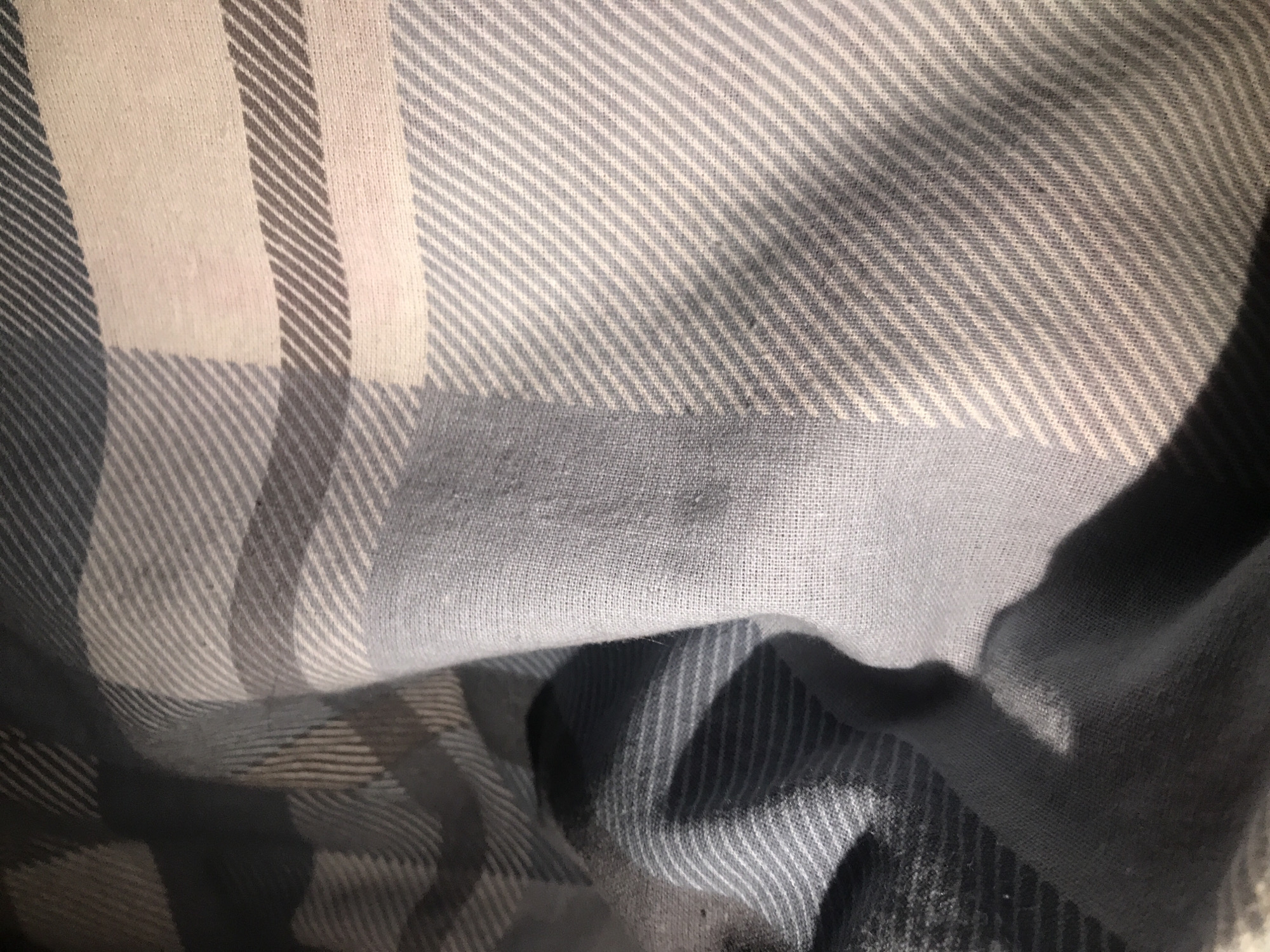 The image shows a close-up of a folded plaid fabric. The fabric has a pattern of intersecting stripes in shades of white, gray, and dark blue. The texture appears soft and possibly cotton. No people or cityscapes are visible, so providing a location like Yerevan, Armenia is not possible based on the visual information in the image.
