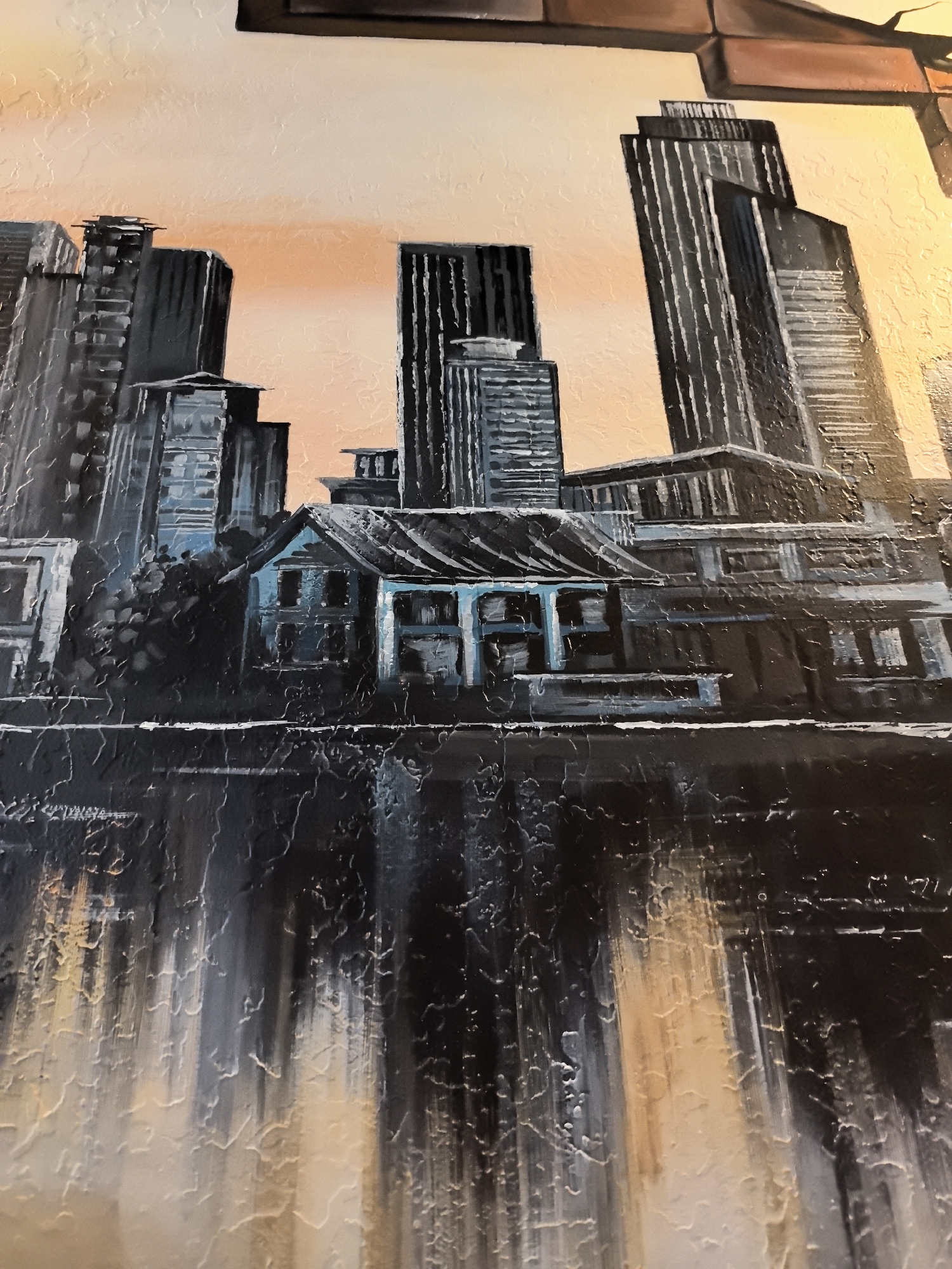 This is a painting of a cityscape at dusk or dawn, with skyscrapers dominating the background and a smaller, older building in the foreground. The sky is a gradient of warm orange and pale yellow, suggesting either sunrise or sunset. The skyscrapers are rendered in dark grays and blacks, with vertical lines emphasizing their height and structure. Some of the skyscrapers have a textured appearance, as if painted with a palette knife.
In the middle ground, a single, blue-tinted building stands out. It appears to be an older, more traditional structure with visible windows and a pitched roof. This building is set against a dark, textured foreground that likely represents water or a dark surface, possibly reflecting the city lights and sky. The reflection is rendered with vertical brushstrokes of black, gray, and hints of the sky's warmer colors, creating a dynamic and abstract effect. The overall style of the painting is expressive and textured, with a focus on light and shadow to create depth and mood. The city appears to be a modern metropolis, possibly a waterfront city, given the reflective surface in the foreground.