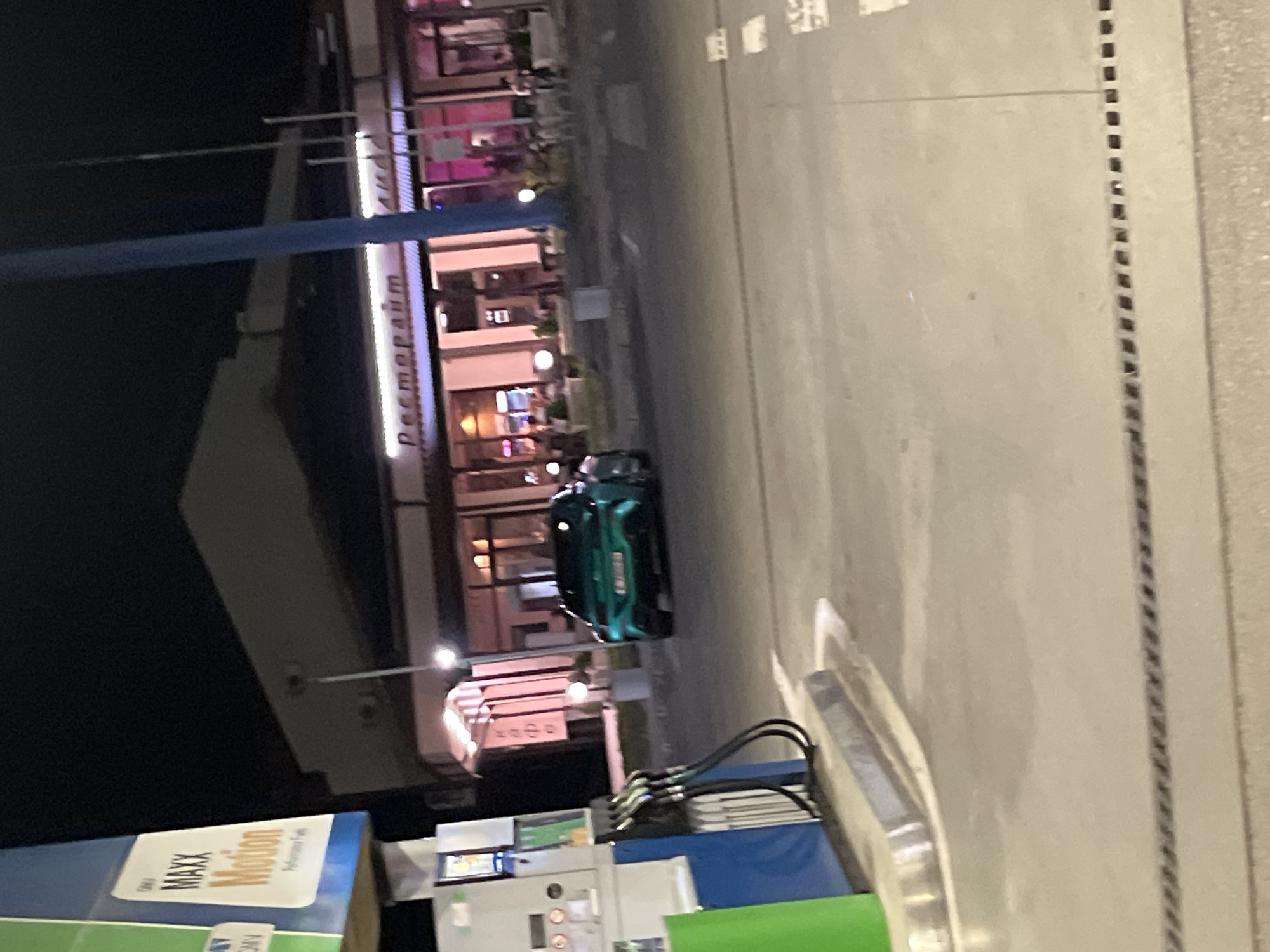 Observed in Popovitsa, Bulgaria, a gas station illuminated at night. A green car is parked near the gas pumps. The "ресторант" (restaurant) sign is visible on a building nearby. Gas pumps are in the foreground, while the lit restaurant facade and parked car are in the background.