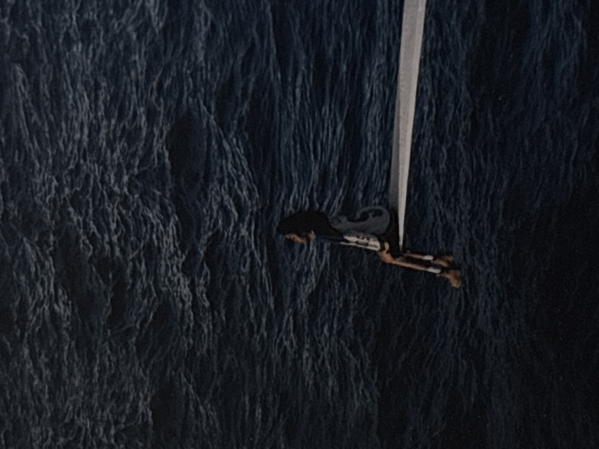A person with dark hair, wearing a jacket and pants, is sitting on the edge of a diving board that extends over dark, rippling water. The person is looking out towards the left of the frame. The water occupies most of the image, appearing calm but with visible movement from waves. The diving board is a light gray color. The scene is captured from an elevated perspective, looking down onto the water and the person. There is no discernible city or urban environment visible.