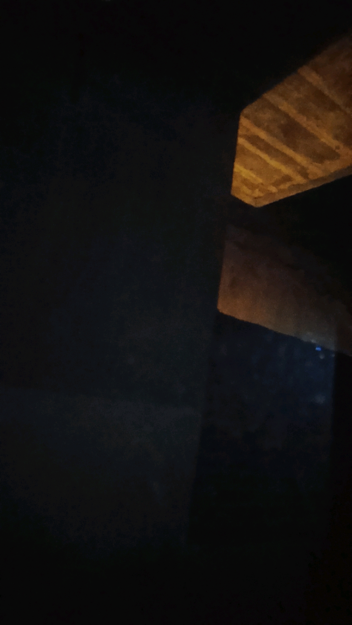The image shows a dark, textured surface, possibly a wall or ceiling, with a section illuminated by a warm, yellow light. The illuminated area reveals parallel lines or ridges on the surface, suggesting it might be made of wood or a similar material. The overall scene is dimly lit, with the bright section providing a stark contrast. There are no people or specific objects clearly identifiable in the image, and no context is provided to determine its location within Ujungrusi, Indonesia.