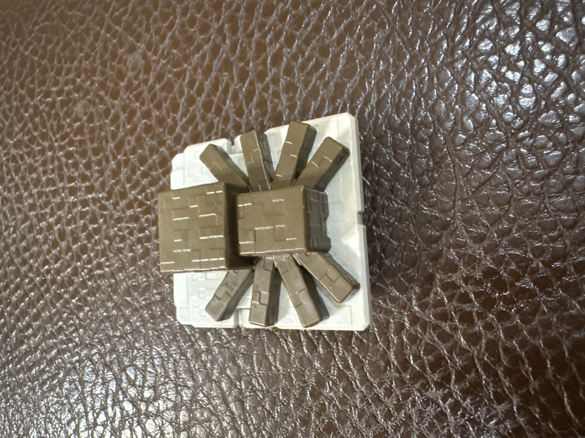 A top-down view depicts a toy structure resembling a Minecraft spider on a textured brown surface. The spider is primarily constructed from square and rectangular blocks in shades of brown and white. The toy is placed on the brown surface, the texture of which resembles leather. No people are visible, and no location or specific details about Yerevan, Armenia, are discernible in the image.