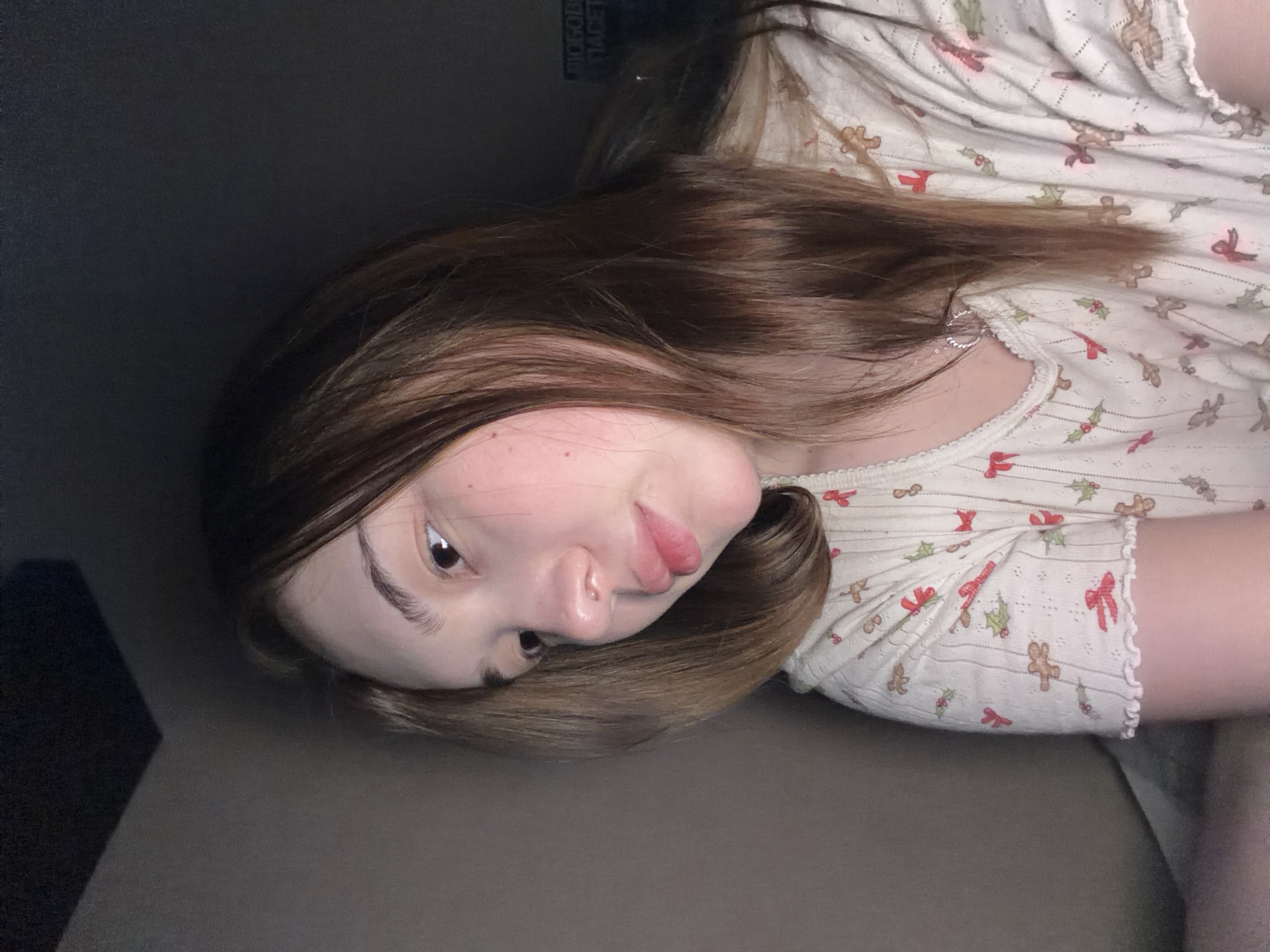 A fair-skinned person with brown hair is lying down. They are wearing a light-colored shirt with holiday-themed patterns. The background is dark and indistinct, suggesting a dimly lit interior. There is no information to indicate that the location is Chaikovsky, Russia.