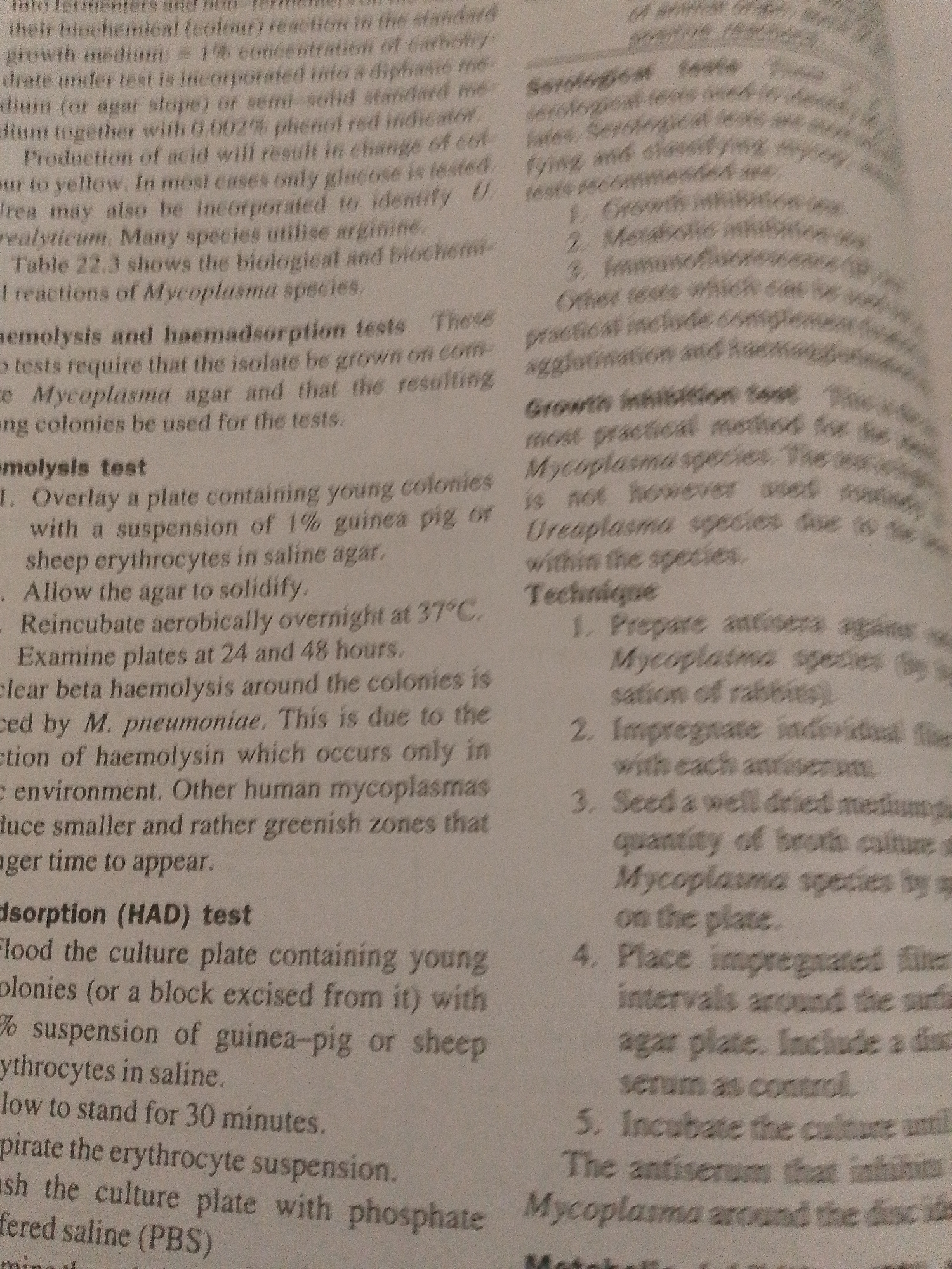 The image is a close-up, slightly blurry photograph of a page from a textbook. The text discusses Mycoplasma and its related tests, including hemolysis and haemadsorption. It also describes serological tests, growth inhibition tests, and metabolic inhibition tests. The page is printed in black ink on white paper. There is no information in the image that relates to Jalingo, Nigeria, or any city.
