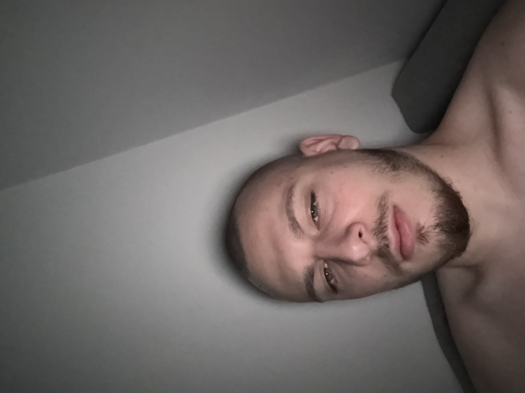 A selfie of a fair-skinned male with a shaved head and a beard. He is lying on a surface next to a wall. There are no other details to identify the location as Stara Zagora, Bulgaria.
