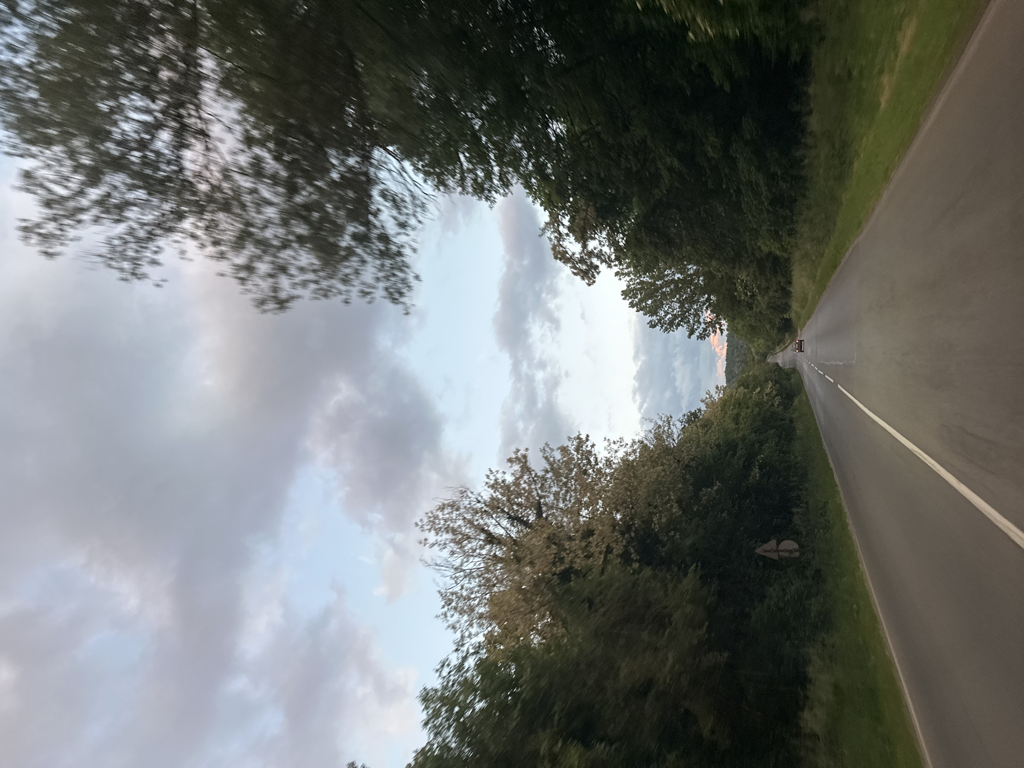A road stretches into the distance, framed by trees on either side. A vehicle is visible in the distance on the road. Above, the sky is filled with clouds. The image suggests a drive through a rural area. The location details (Pryaporets, Bulgaria) are not visually discernible in the image.