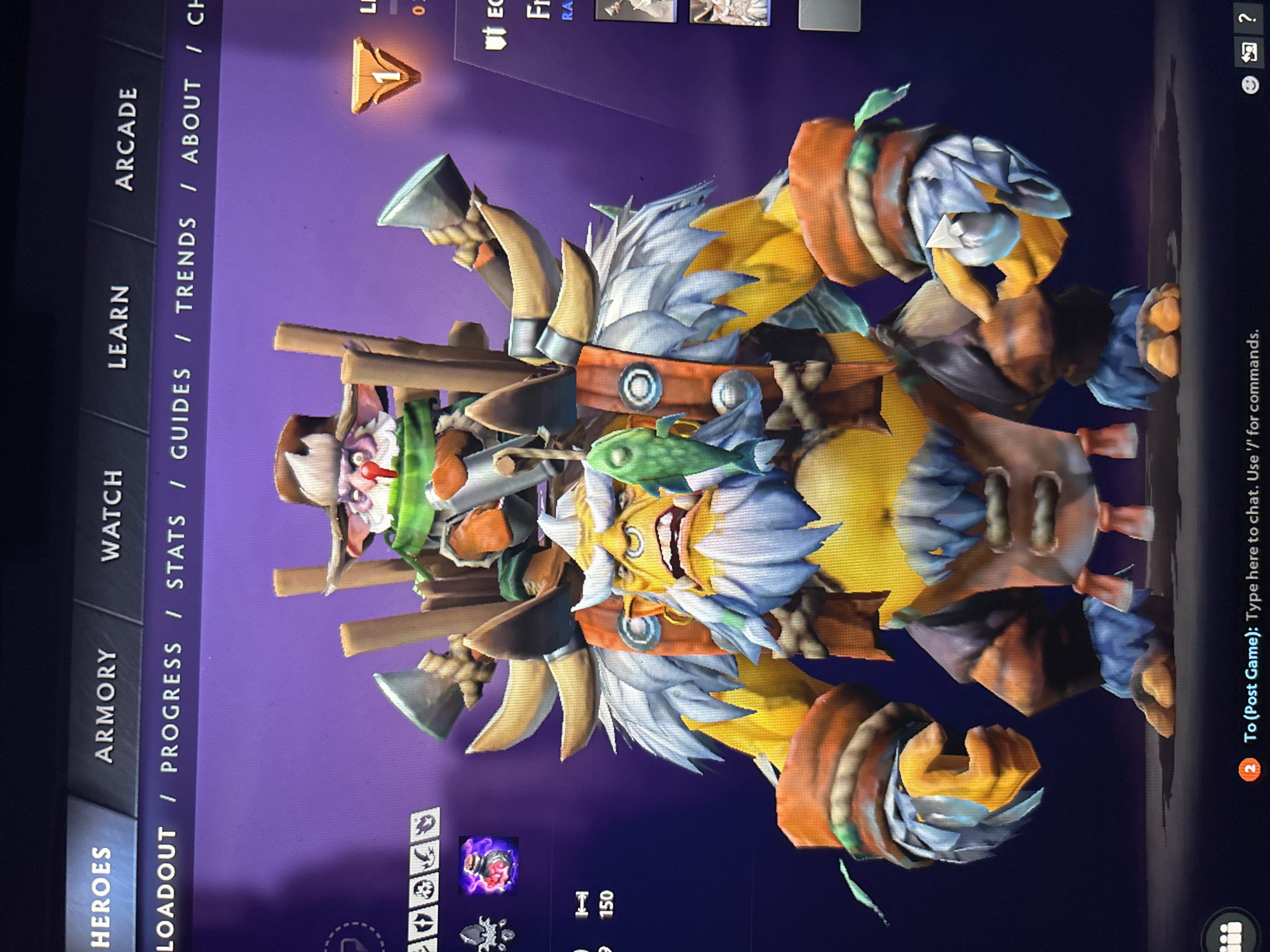 The image displays a vertical photograph of a computer screen showcasing a video game interface, likely from Dota 2. The central subject is a brightly colored, stylized video game character, a large humanoid figure with a yellowish body, prominent white spiky hair or fur, and a wide, toothy grin. It is adorned with an orange belt, large orange armbands, and blue-grey armored details on its limbs. Accessories include large tusks, wooden planks, small axes, and a green fish-like object. A smaller, distinct creature with a white face, red nose, green scarf, and a hat is perched near the main character's left shoulder.
The background behind the character is a solid purple. The screen is filled with user interface elements from the game. Along the left edge (top of the image), navigation tabs are visible, reading "HEROES," "ARMORY," "WATCH," "LEARN," and "ARCADE." Below these, another set of tabs states "LOADOUT / PROGRESS / STATS / GUIDES / TRENDS / ABOUT / CH" (partially obscured). In the bottom right corner (top right of the image), a chat box provides instructions: "2 To (Post Game): Type here to chat. Use '/' for commands." Other visible text and numbers include "LI," "Fr," "RA," "150," and a level indicator showing "1." The image captures a static display of the character within the game's menu system, rather than active gameplay. No specific time of day, weather, or physical location is discernible from the digital content.