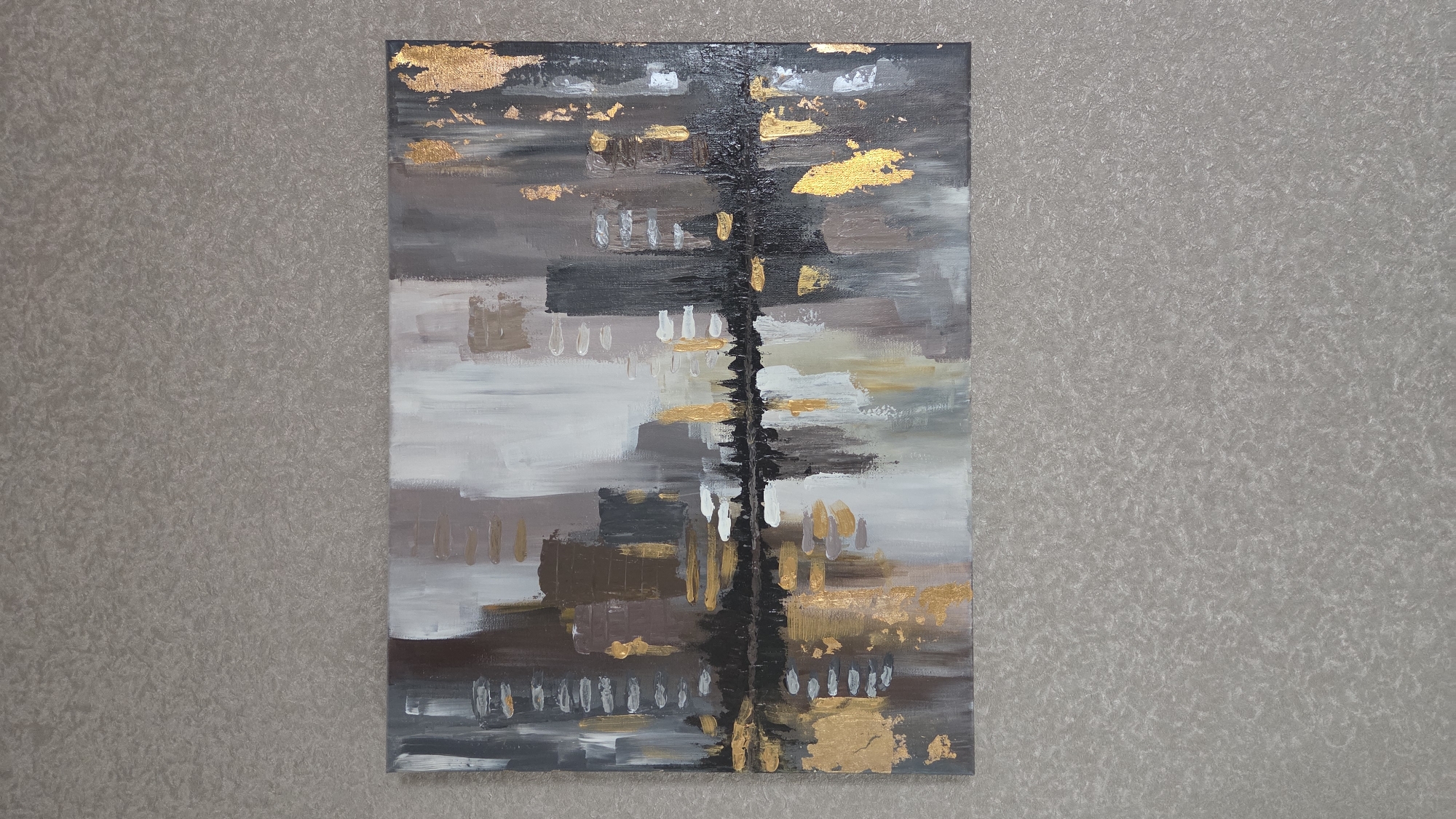 The image shows an abstract painting hanging on a wall with a textured gray wallpaper. The painting features a vertical black stripe down the center. It's composed of various horizontal brushstrokes in shades of gray, white, brown, and gold. The gold appears as small, irregular patches scattered throughout the painting. The painting is vertically oriented and takes up a significant portion of the frame. The specific location within Chaikovsky, Russia, cannot be determined from the given image alone.